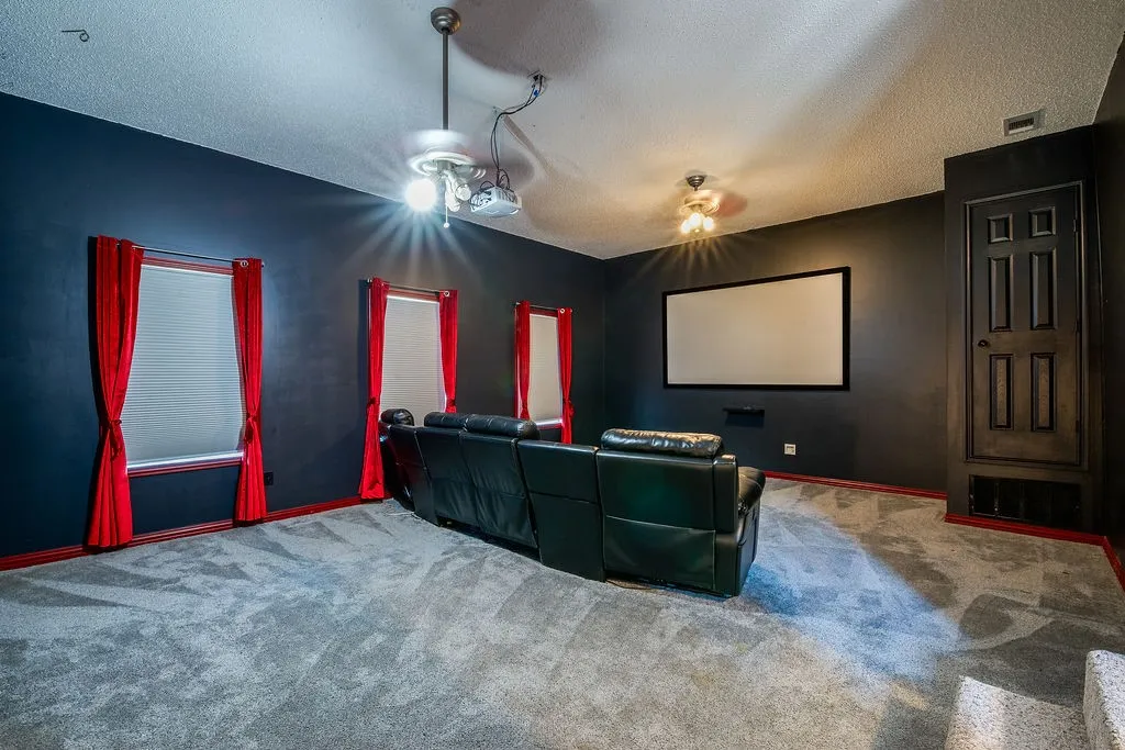 Dedicated media room featuring a large projection screen, dark wall finishes, and gray carpet flooring