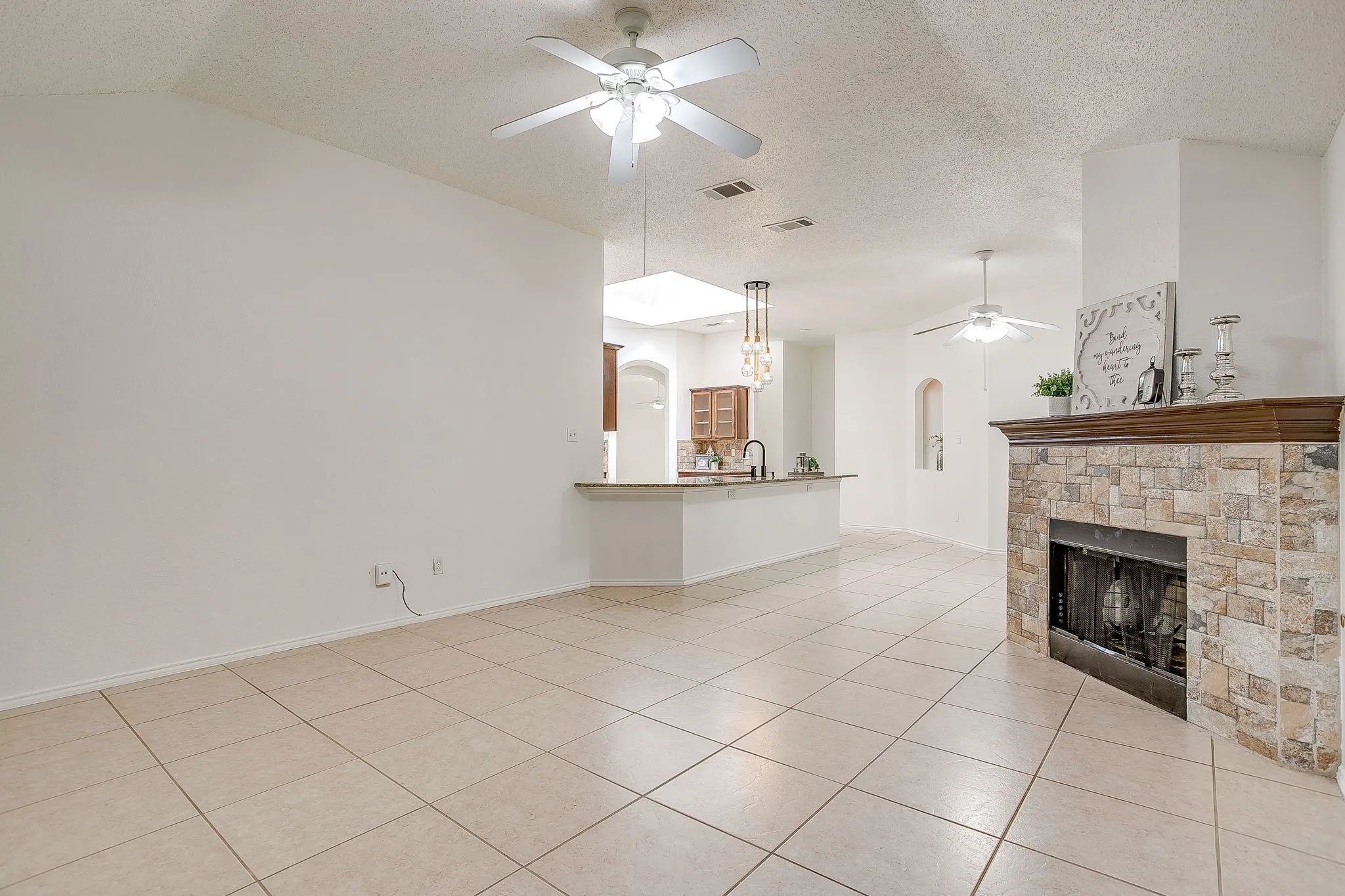 The living room featuring light-toned tile flowing seamlessly into the dining area and kitchen.