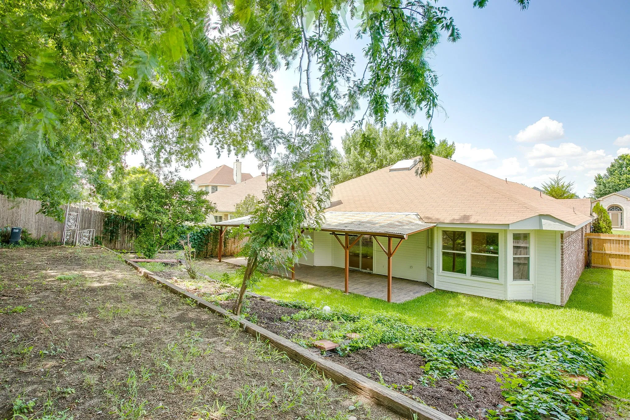 The rear exterior view of the home featuring the garden and shade trees.
