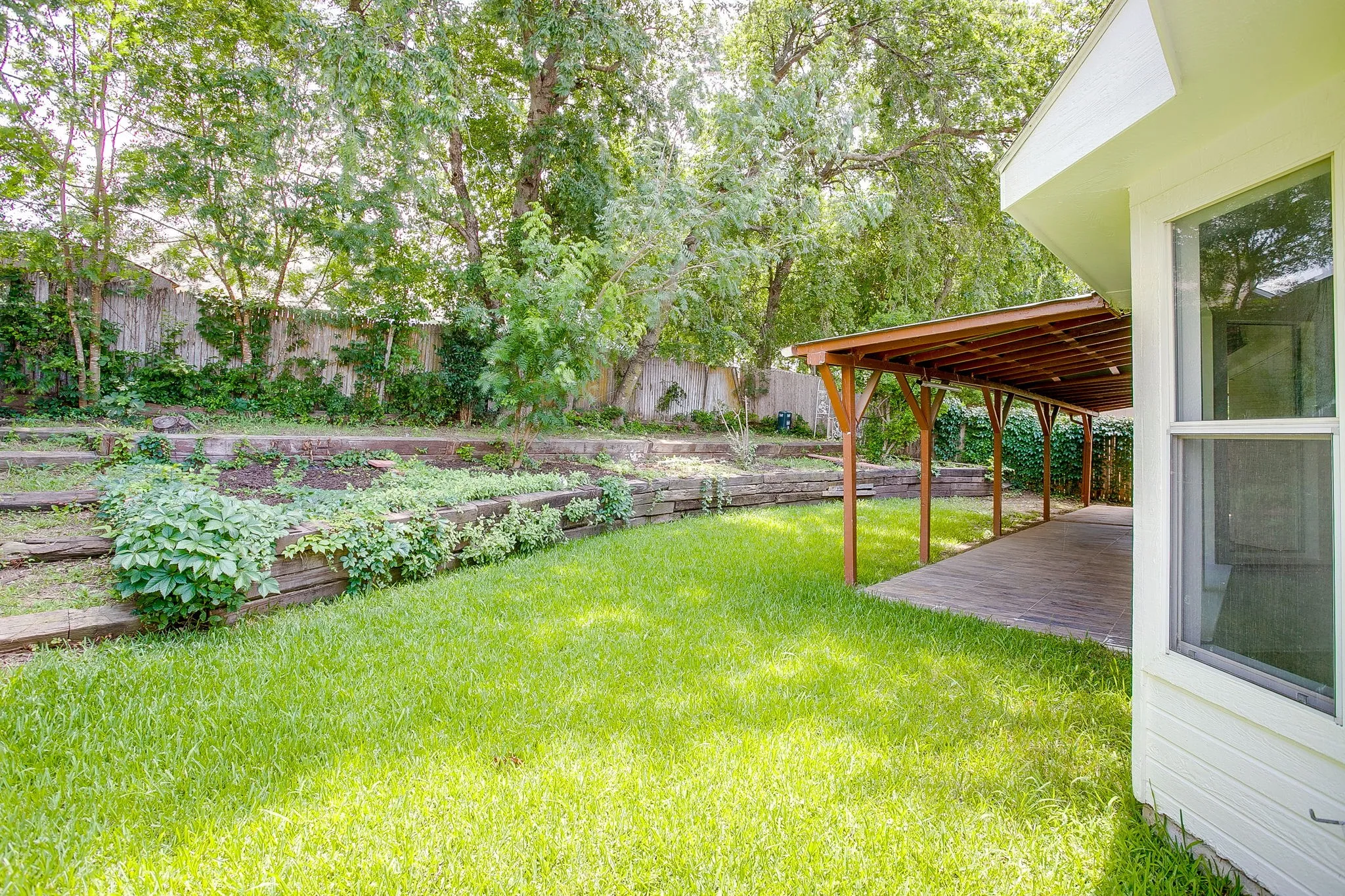 The backyard featuring terraced flower beds and large shade trees.