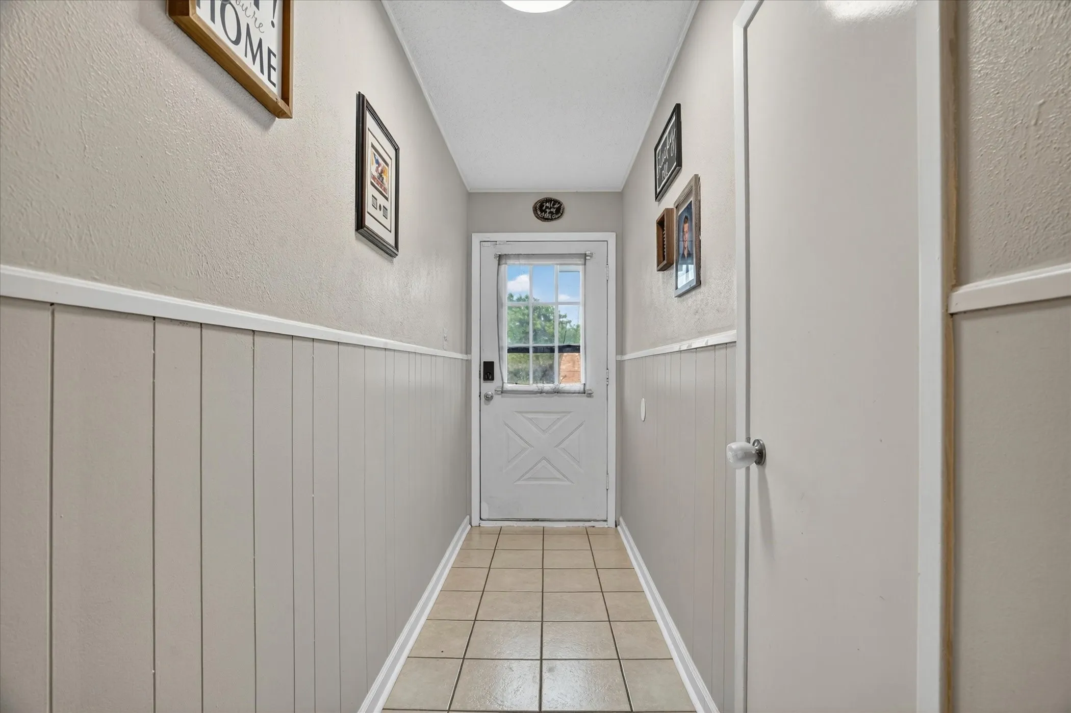 Hallway featuring beadboard wainscoting, neutral paint, ceramic tile flooring, and a rear exterior door with integrated window