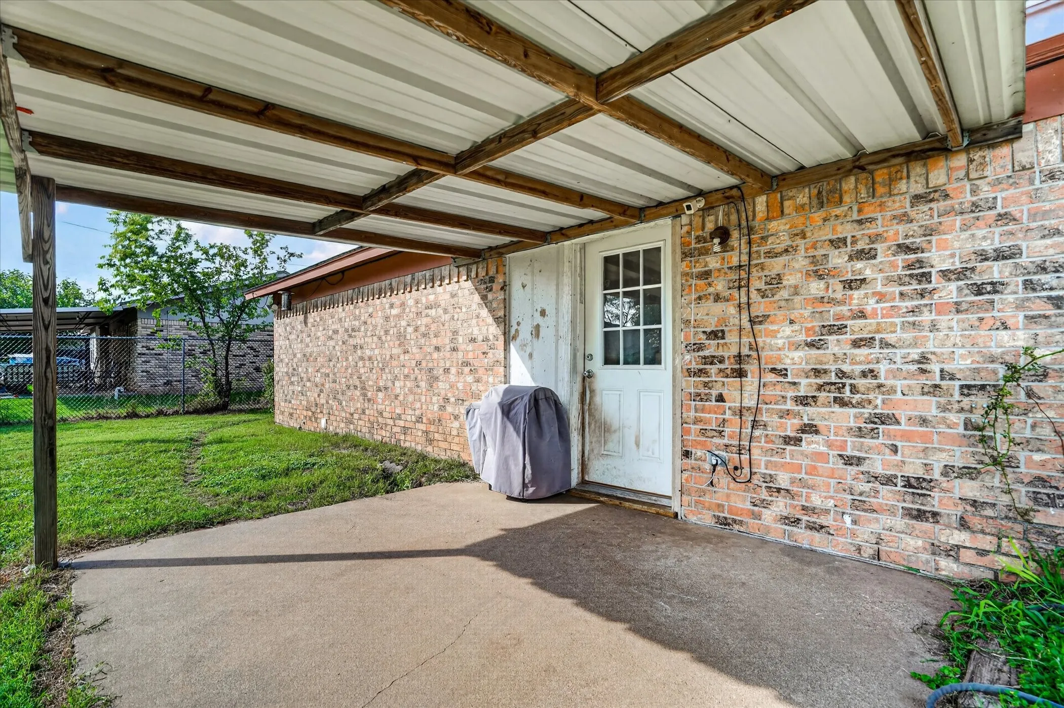 Covered concrete patio with a tin roof structure supported by wood beams and posts