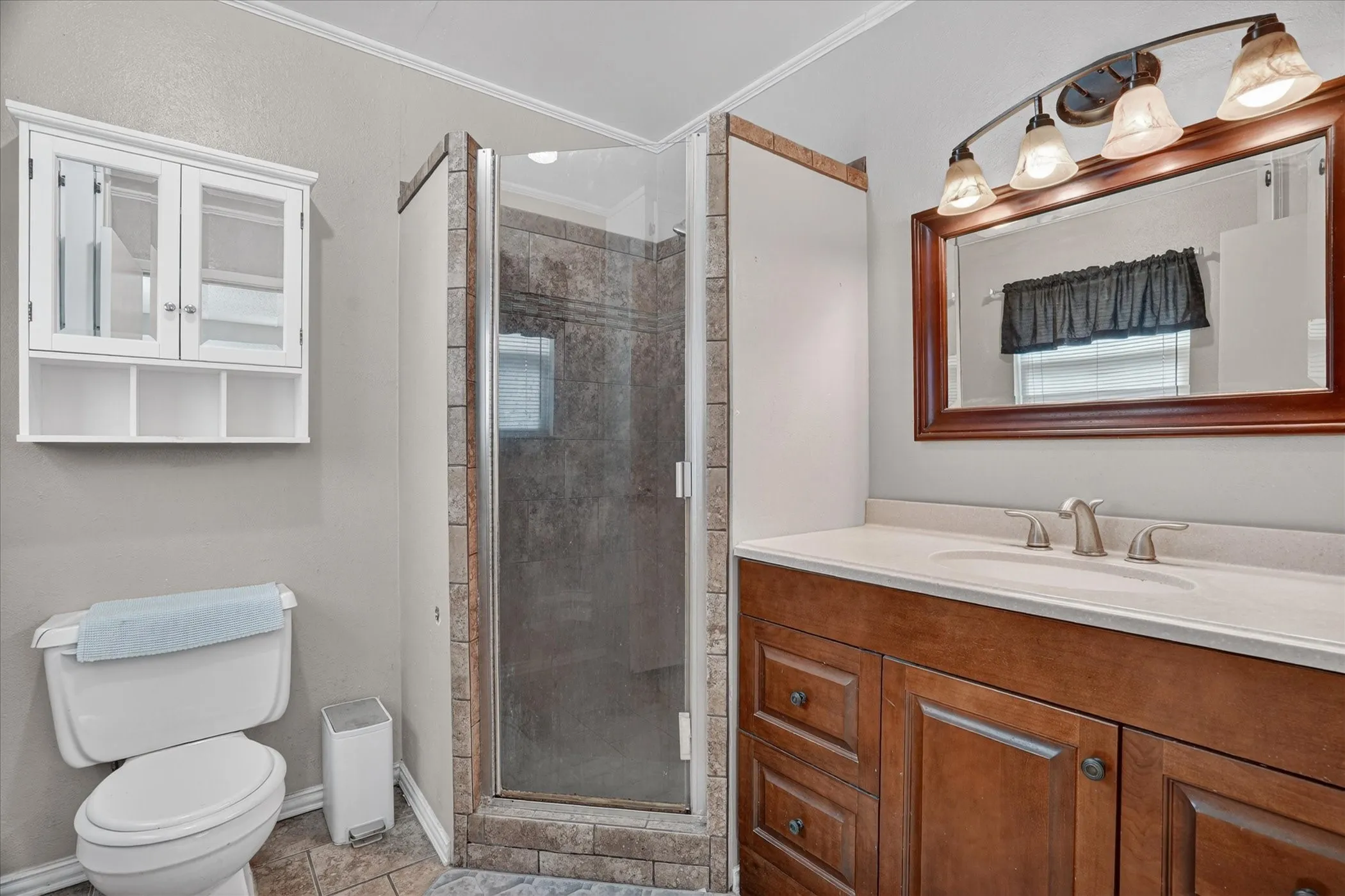 Shower enclosure with tiled surround, a wood-finish vanity with an integrated sink, and a decorative mirror with a four-light fixture