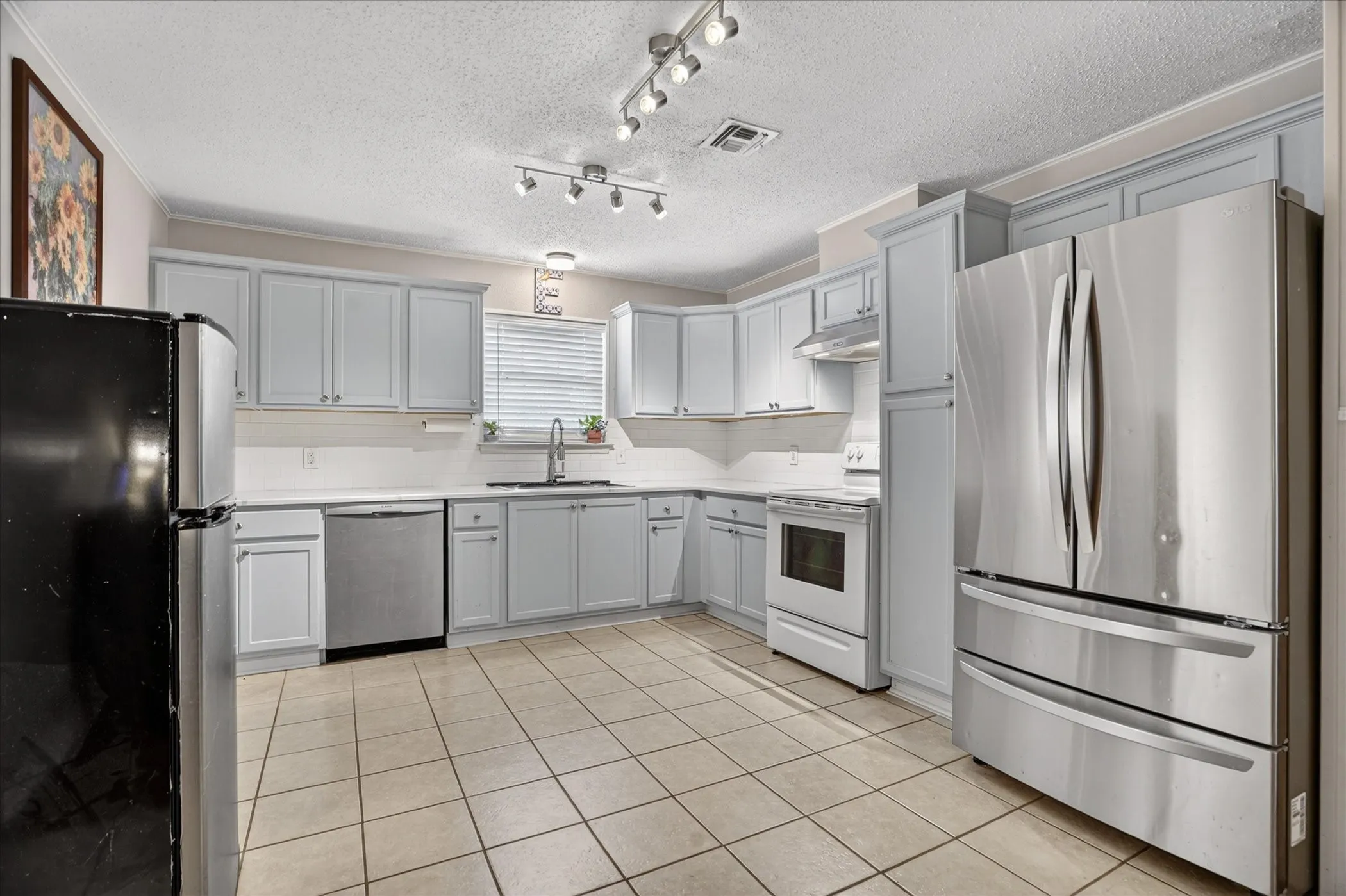 Spacious kitchen featuring light gray cabinetry, white countertops, tile flooring, and a stainless steel refrigerator