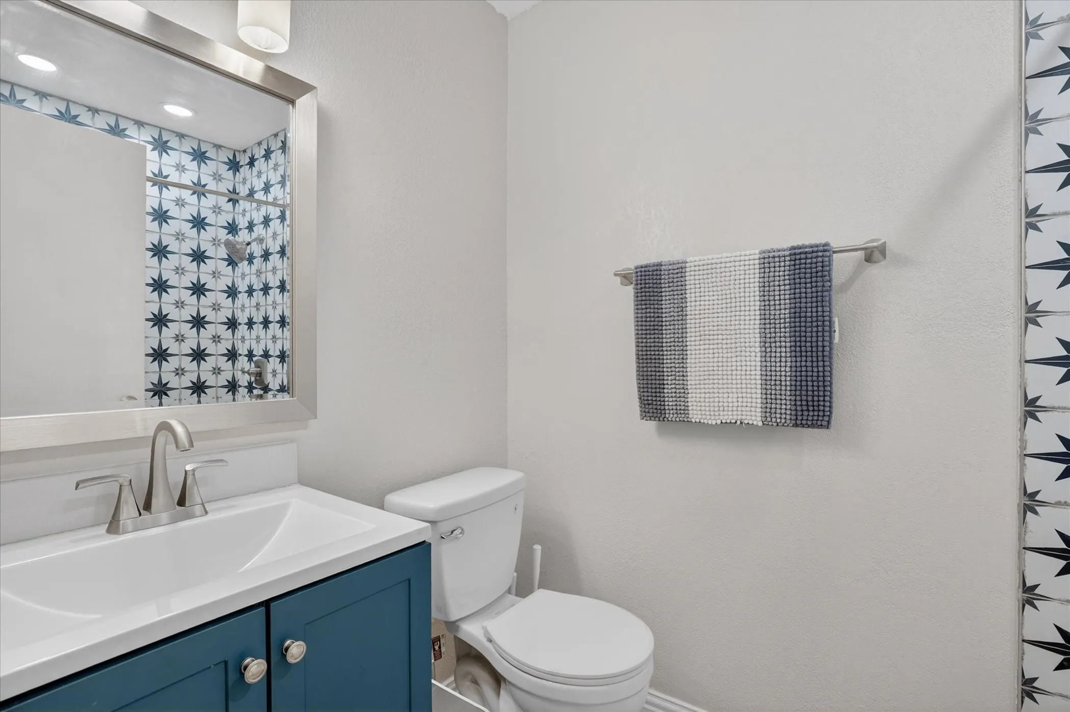 Bathroom featuring a vanity with a white countertop and blue cabinetry, a toilet, and patterned tiled walls