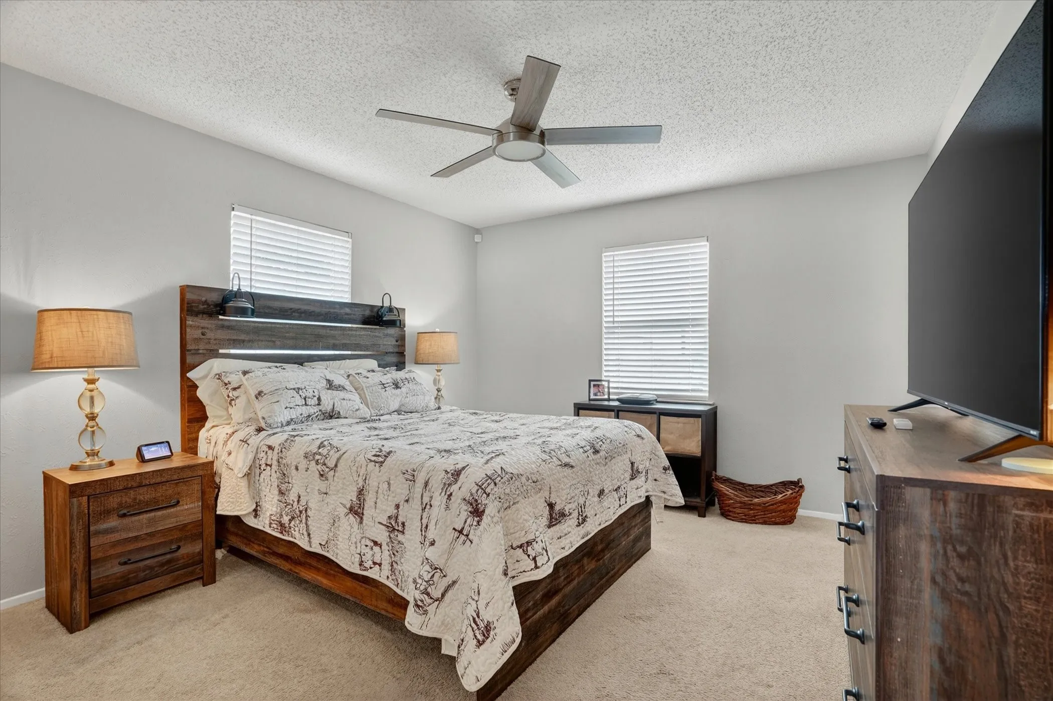 Carpeted bedroom featuring neutral wall tones, two windows with blinds, a ceiling fan with integrated lighting, and ample space for furnishings