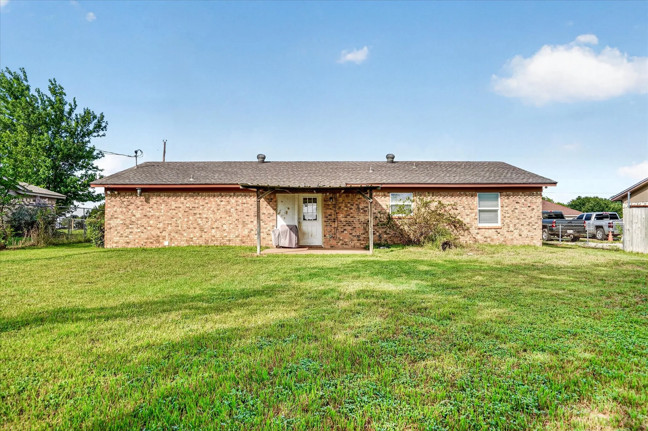 Expansive lawn area featuring a brick exterior, shingle roof, and a covered patio space