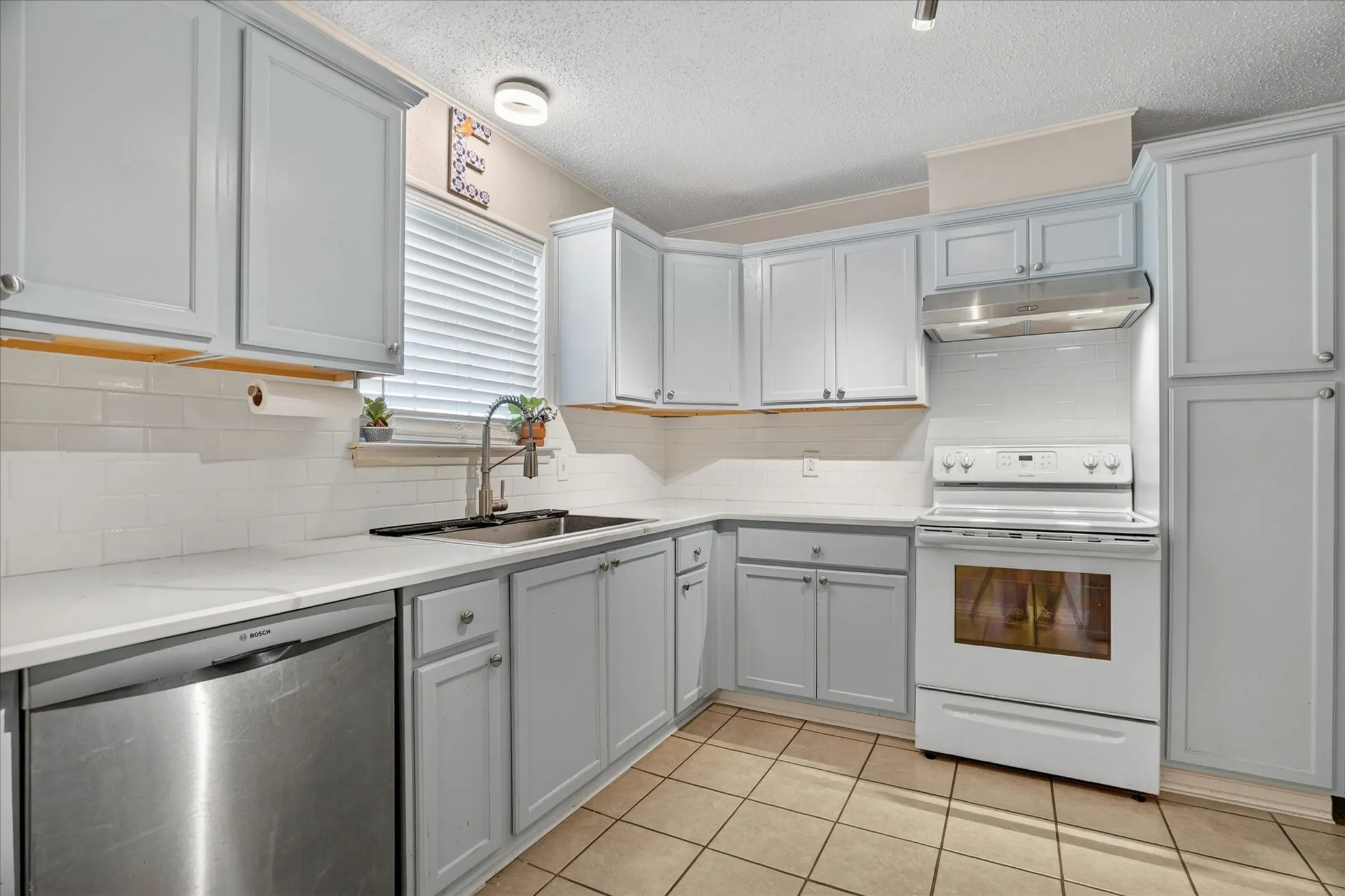 Kitchen featuring light gray cabinetry, white subway tile backsplash, white countertops, and tile flooring
