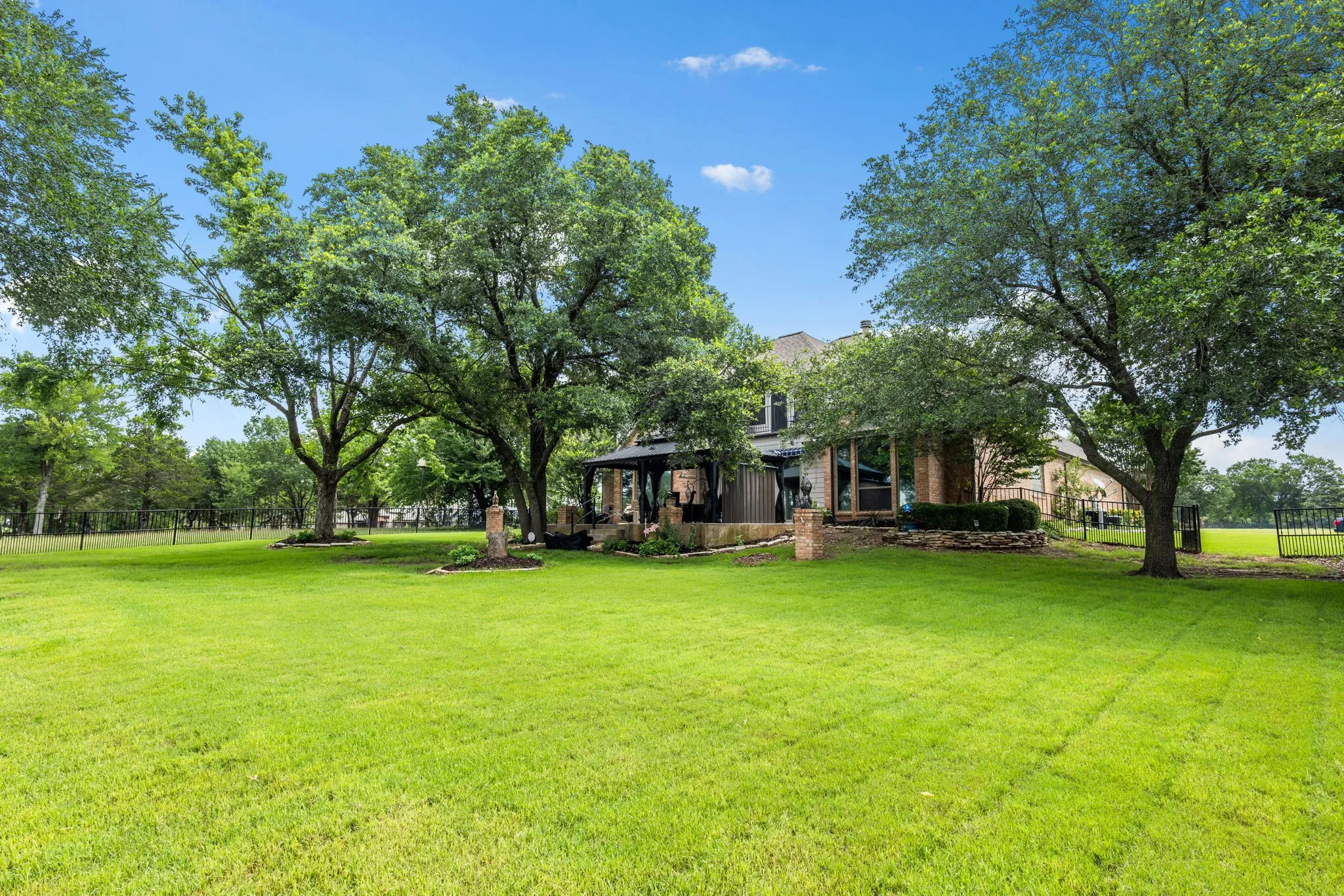 Expansive green lawn with mature trees and a brick-clad residence in the background