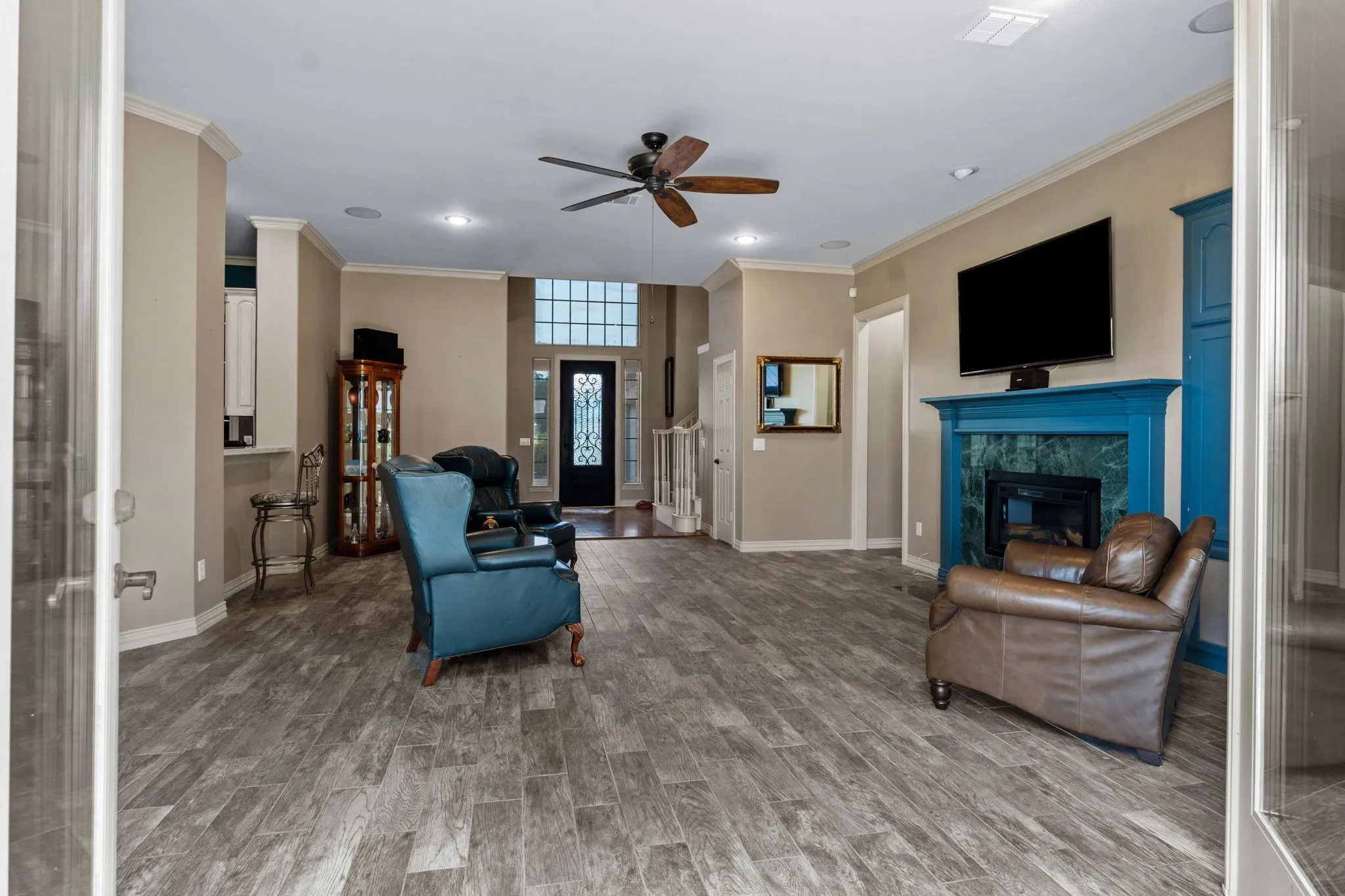 Spacious living area featuring wood-finish flooring, a vibrant blue fireplace mantel with a dark tile surround, and crown molding