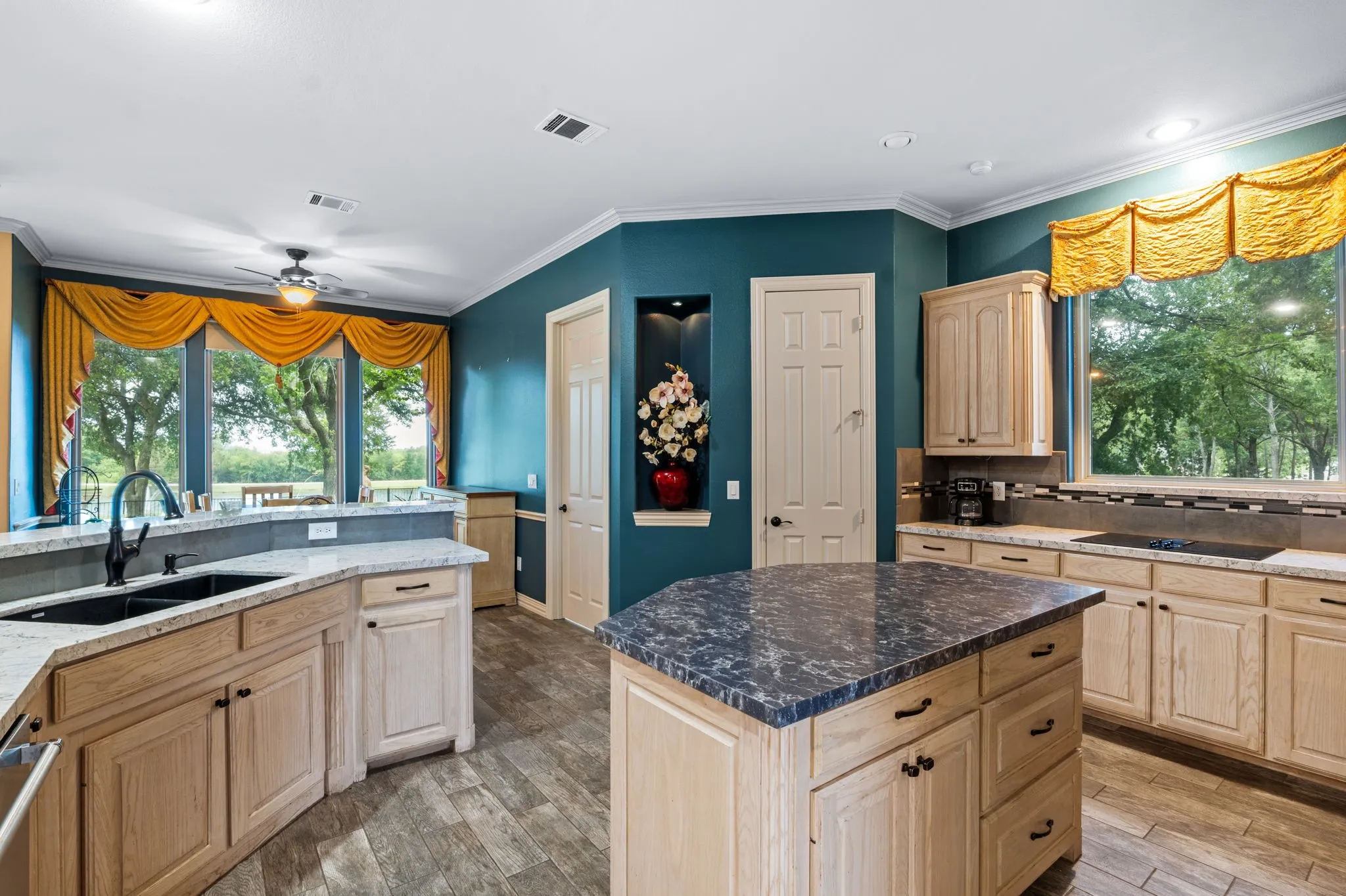 Spacious kitchen featuring wood-finish flooring, light wood cabinetry, stone countertops, and a central island with a contrasting stone surface