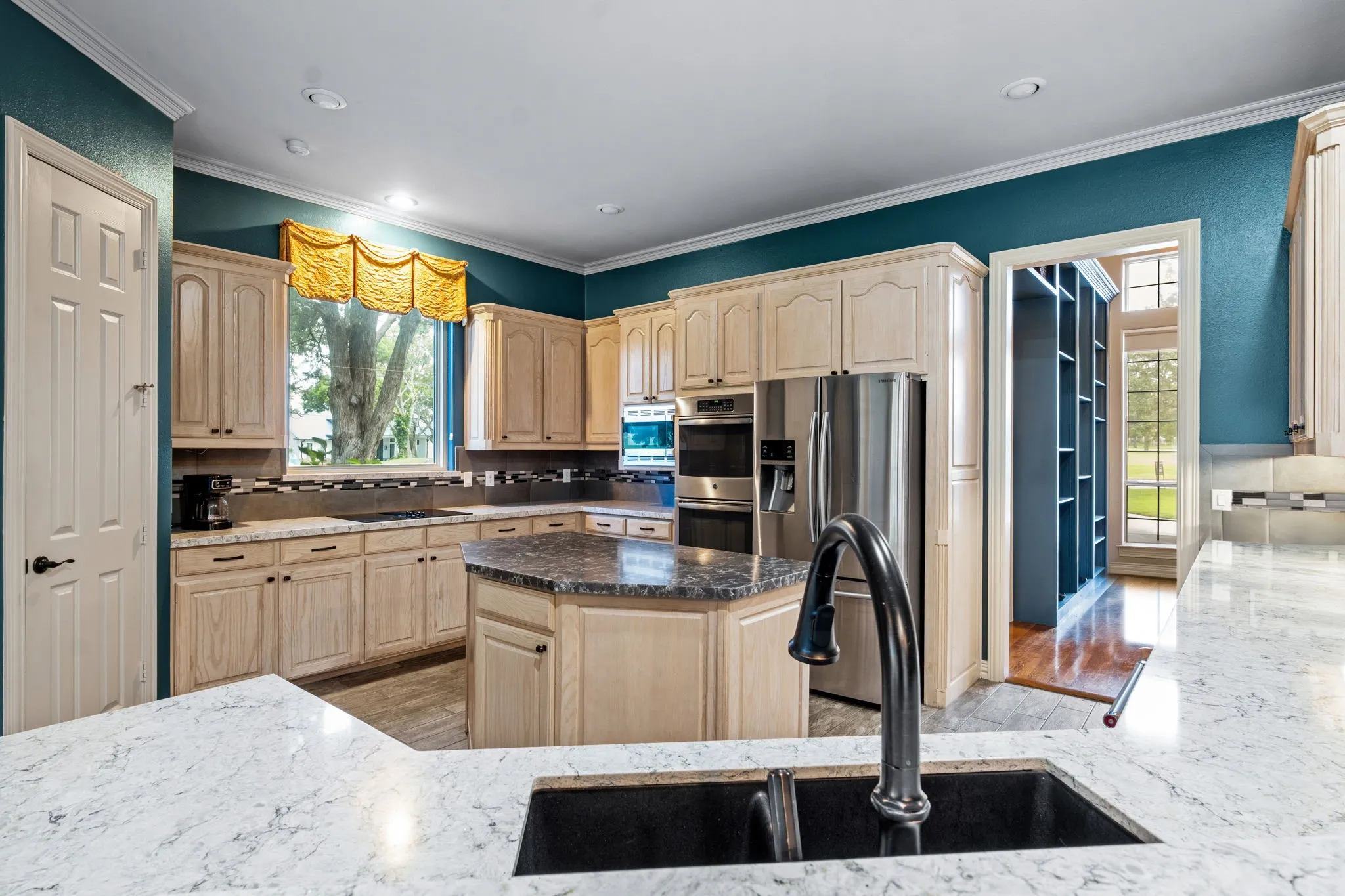 Kitchen featuring ample light wood cabinetry, stainless steel appliances, a center island with a dark stone-finish countertop, and white stone-finish perimeter countertops