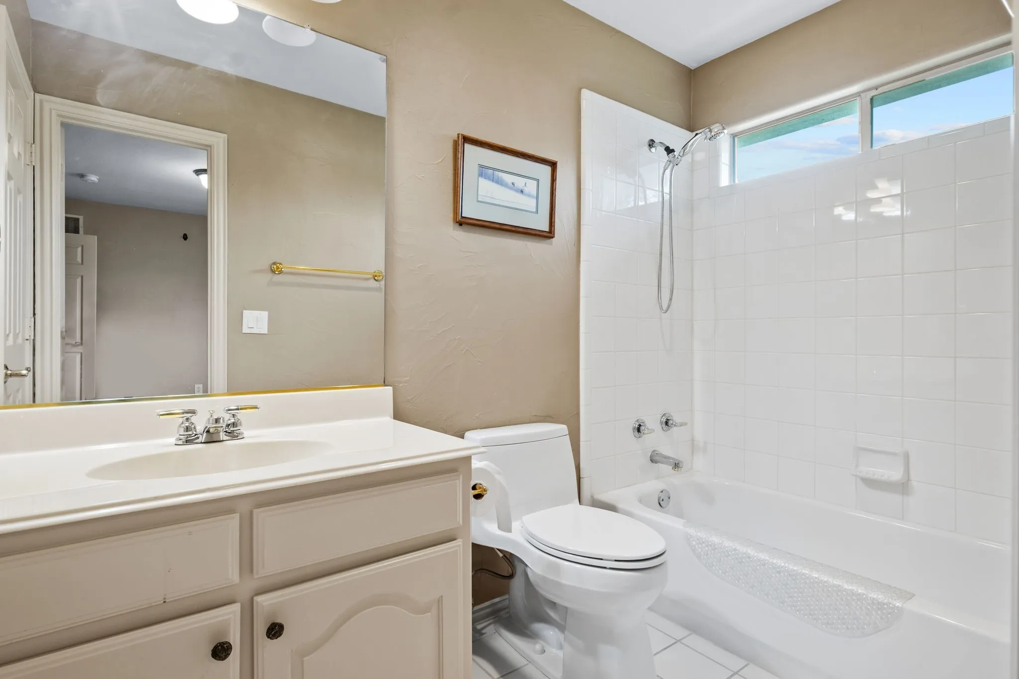Bathroom featuring a built-in vanity with an integrated sink, a white bathtub with subway tile surround, and an upper window providing natural light