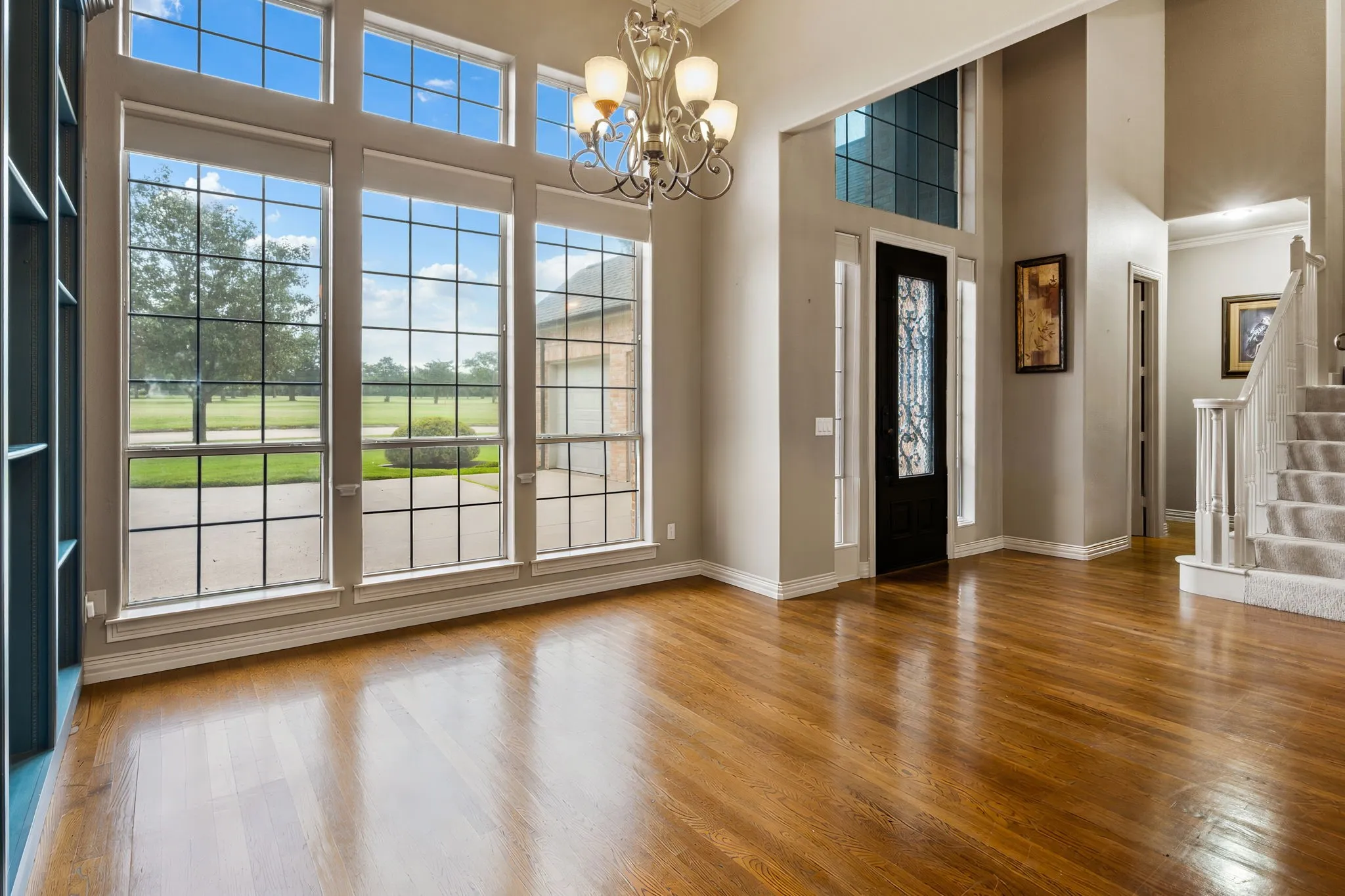 Two-story foyer with rich wood-finish flooring, a grand chandelier, and a prominent black entry door with decorative glass