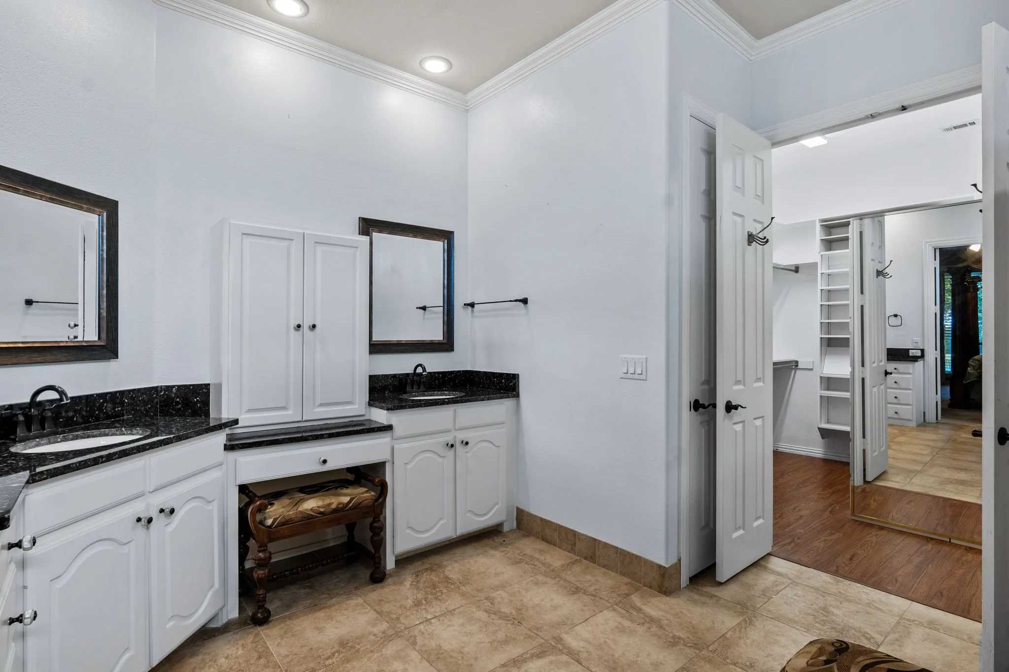 Bathroom featuring dual vanity areas with dark granite countertops, undermount sinks, and white cabinetry