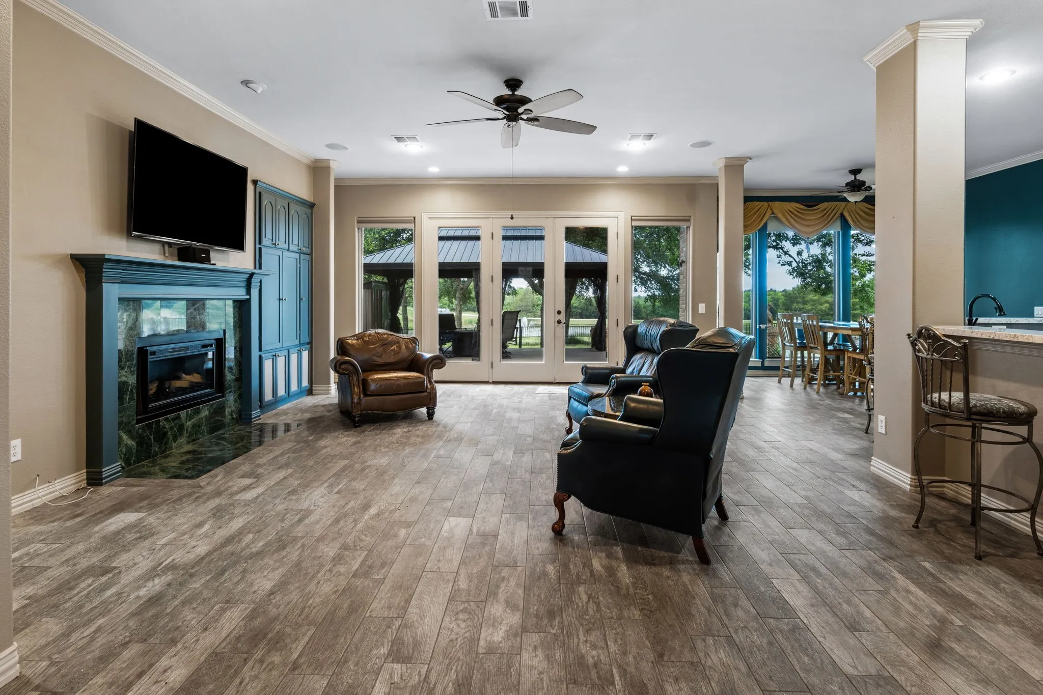Spacious living area featuring wood-finish flooring, a fireplace with a stone surround and ornate mantel, built-in cabinetry, and multiple glass-paneled doors with transom windows