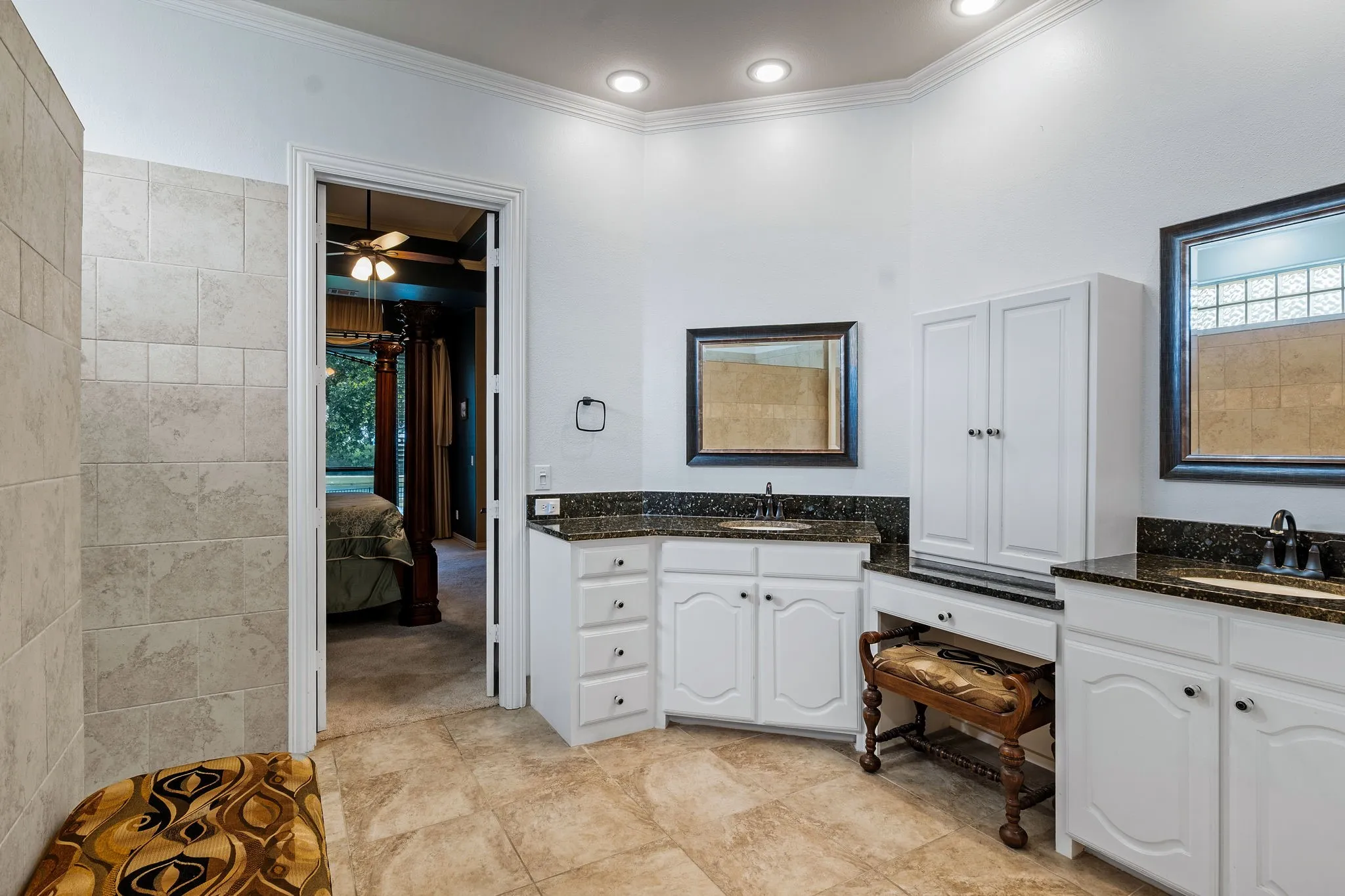 Spacious bathroom featuring dual vanities with dark countertops, white cabinetry, and recessed lighting