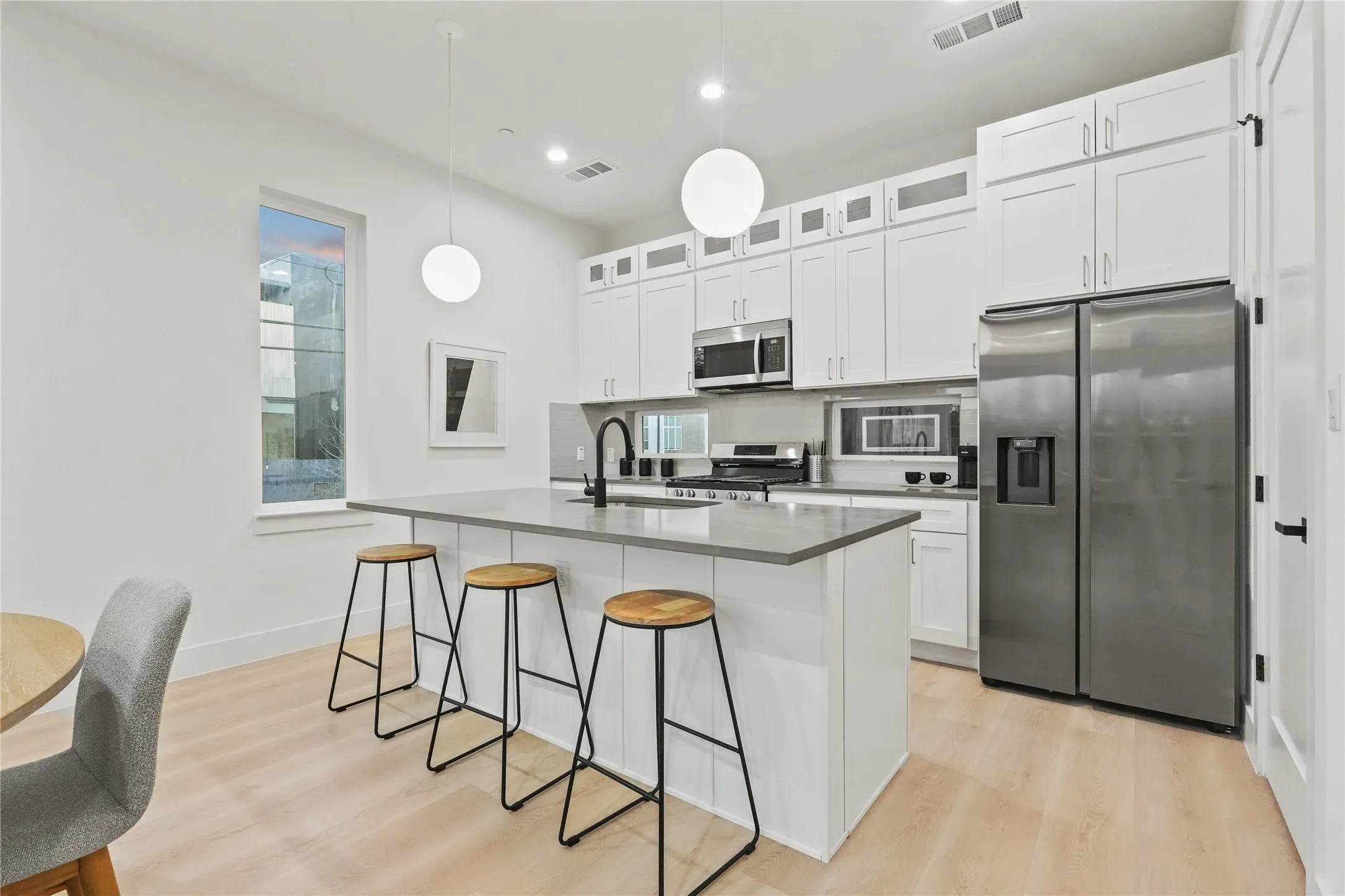Kitchen featuring stainless steel appliances, white cabinetry, light wood-style floors, glass insert cabinets, and a kitchen bar