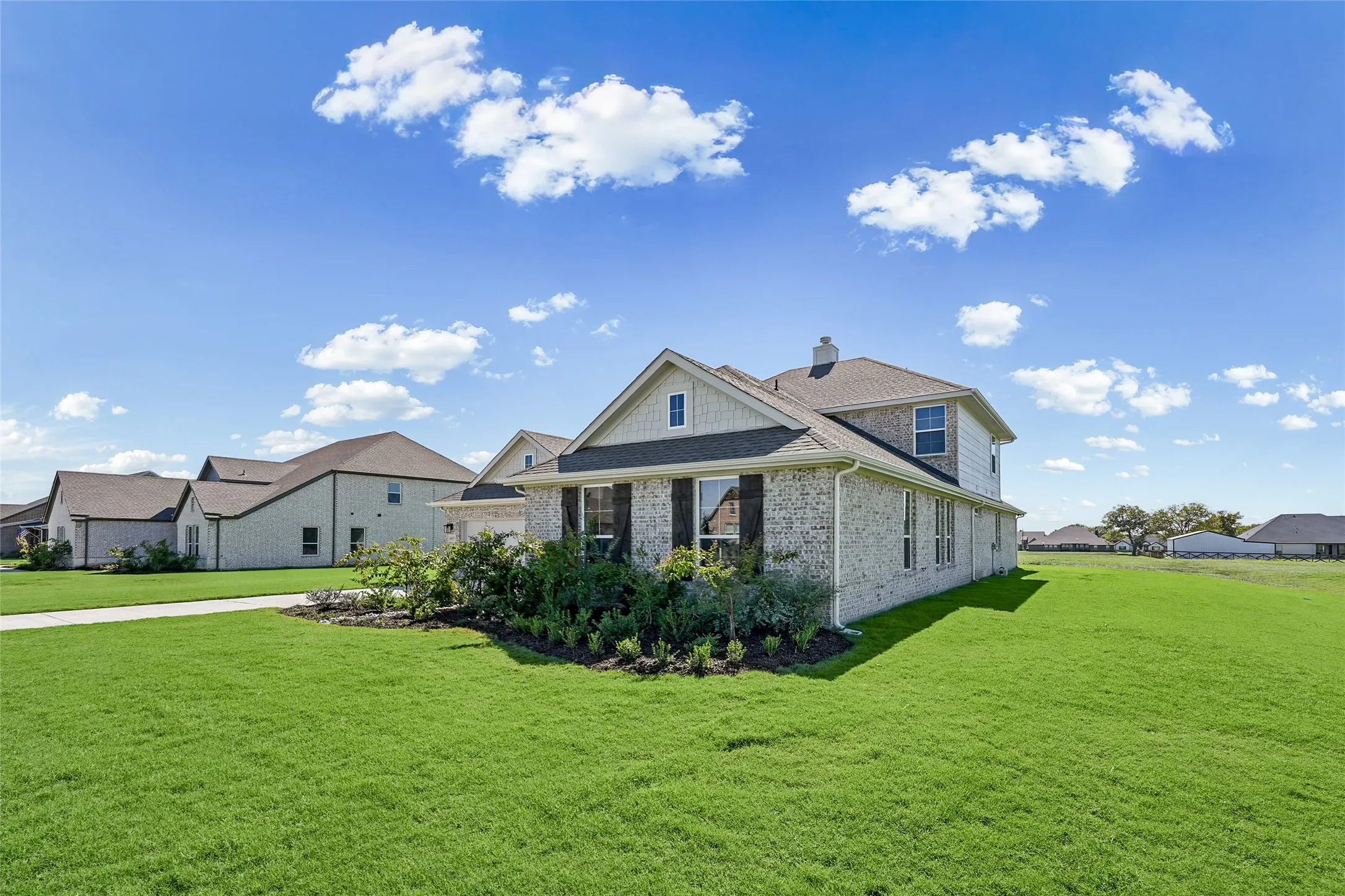 Brick exterior, dormer window, established landscaping, attached garage, and a lush green lawn