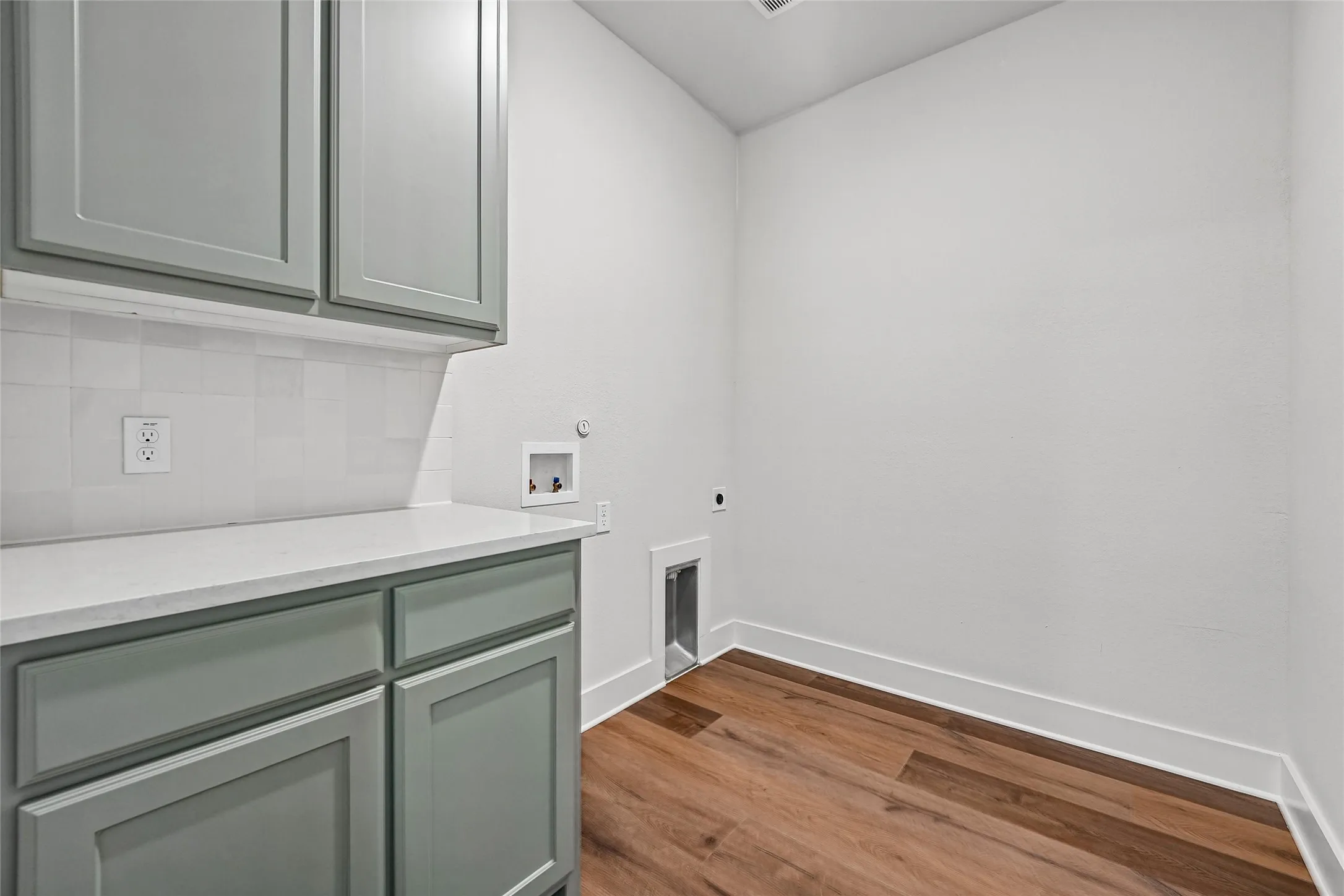 Sage green cabinetry with a white countertop, white subway tile backsplash, wood-finish flooring, and white baseboards