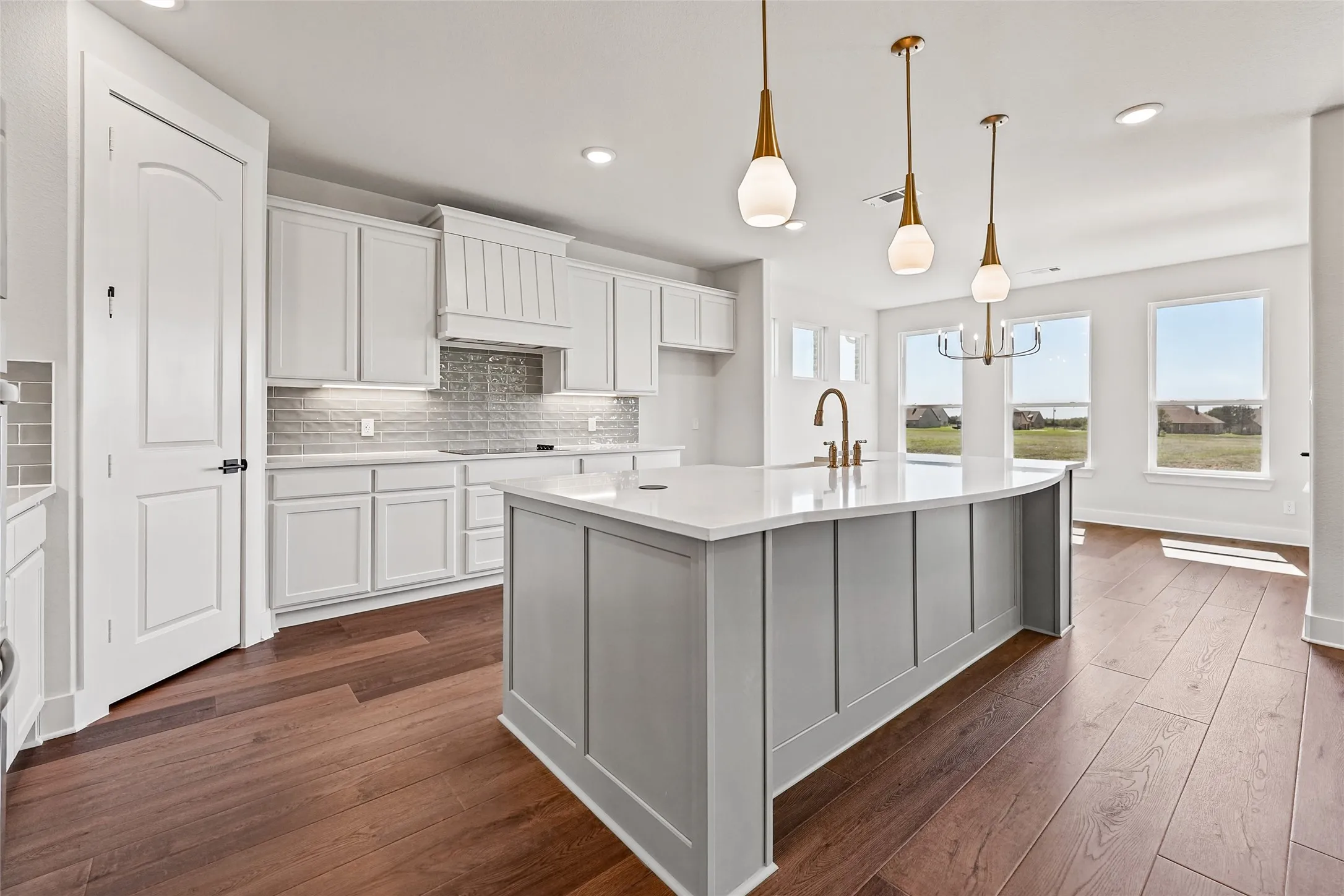 Spacious kitchen featuring white cabinetry, gray subway tile backsplash, a large center island with a sink, and wood-finish flooring throughout