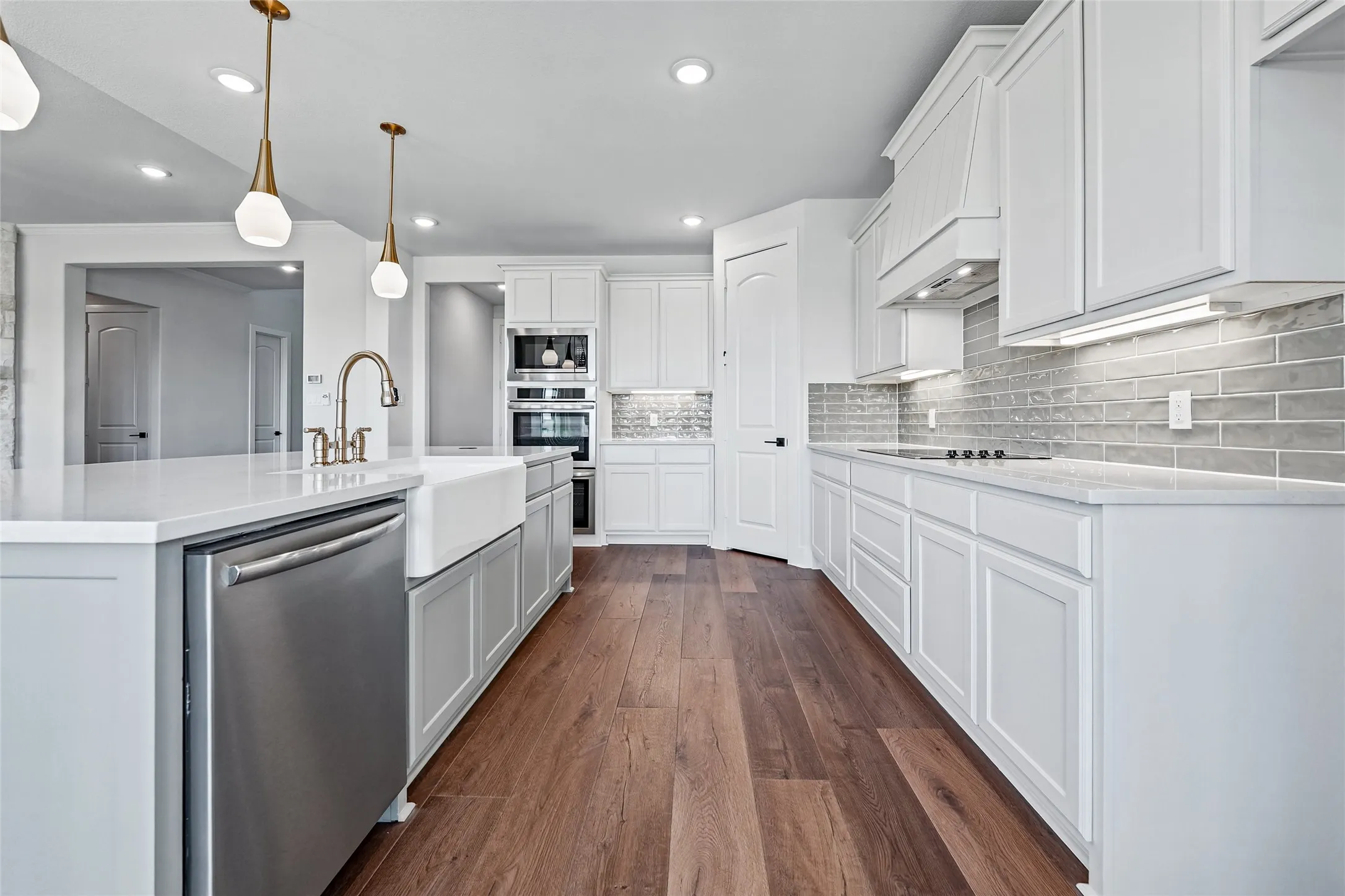 Bright kitchen with wood-finish flooring, white cabinetry, integrated stainless steel appliances, a large center island, and subway tile backsplash