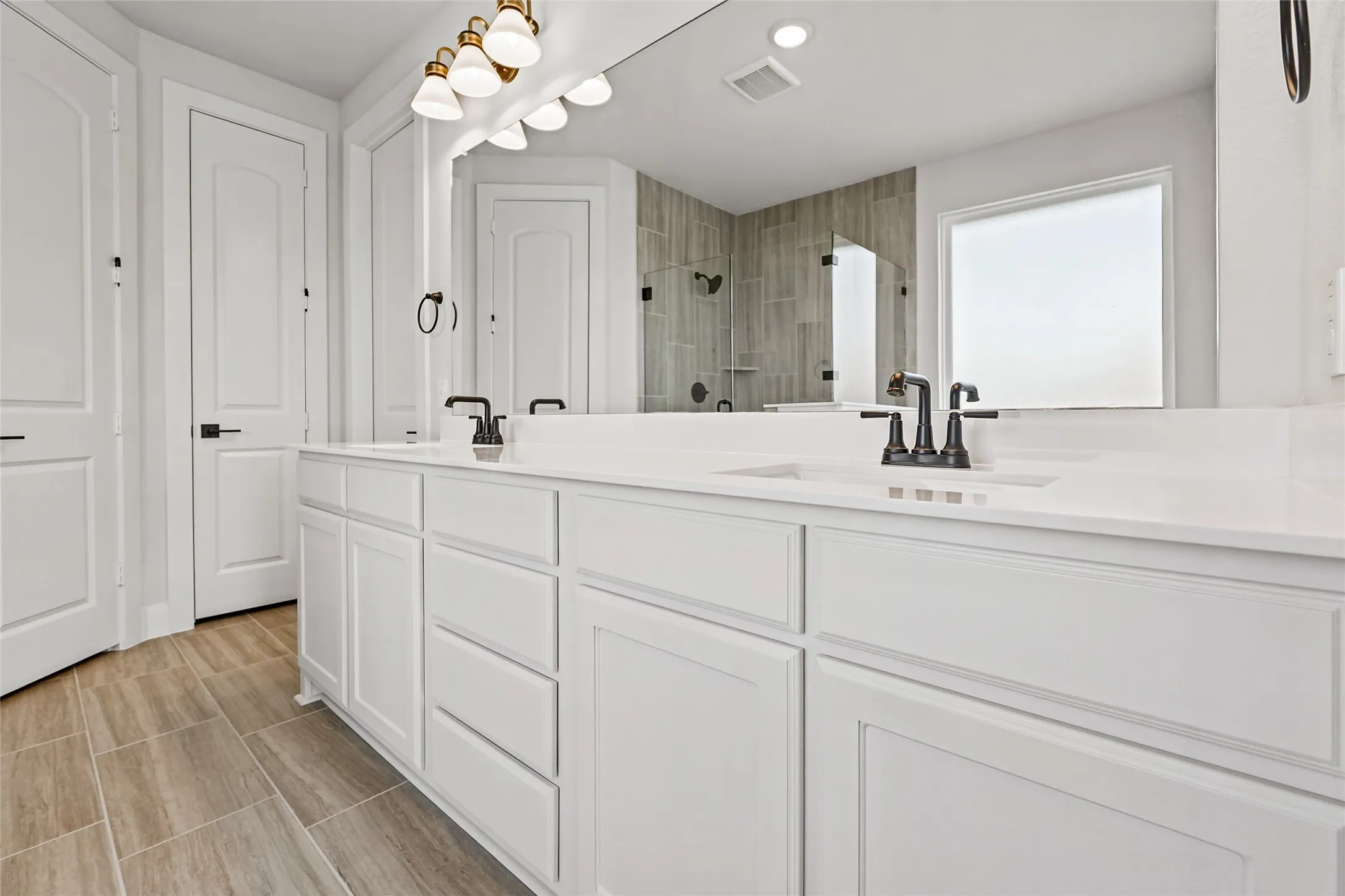 Dual vanity with white cabinetry and integrated sinks, matte black plumbing fixtures, large framed mirror, and wood-finish tile flooring
