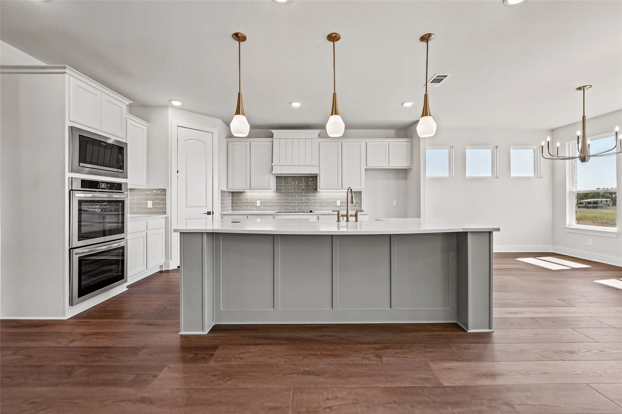 Spacious kitchen with a large central island, integrated stainless steel appliances, wood-finish flooring, and pendant lighting fixtures