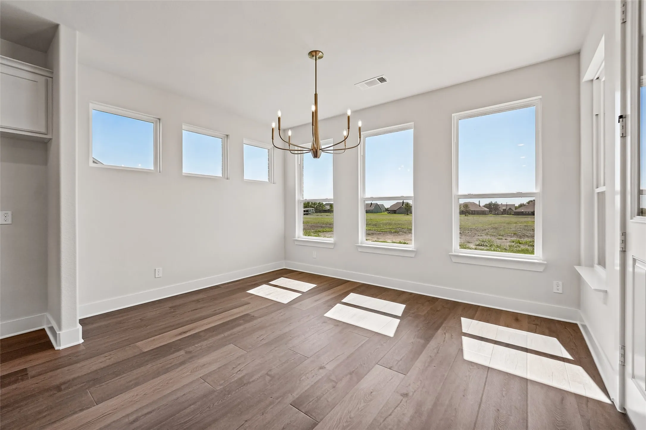 Hardwood-style flooring, white walls, multiple windows, built-in shelving, and a gold-finish chandelier