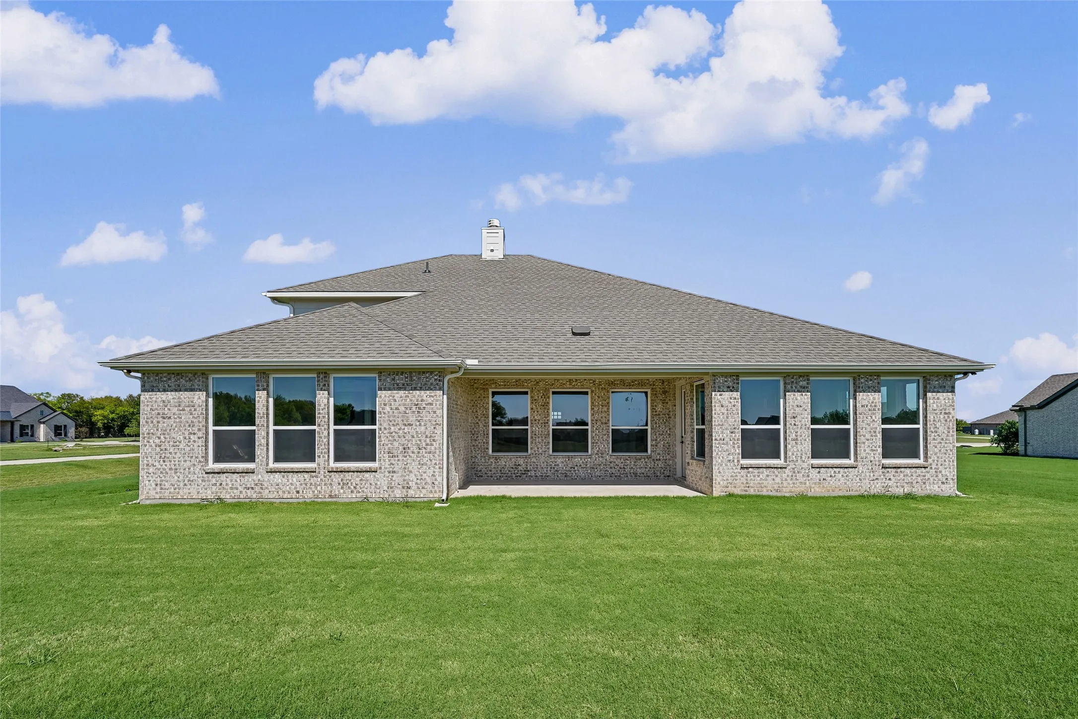 Expansive green lawn with a covered concrete patio, light-colored brick exterior, and multiple windows
