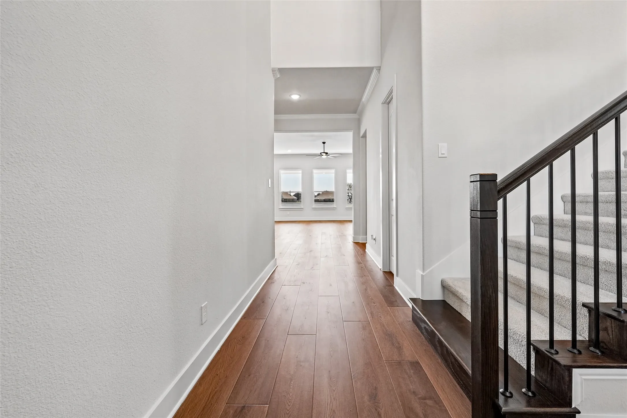 Wood-finish flooring throughout, bright white walls, recessed ceiling lighting, and dark wood staircase with wrought iron balusters