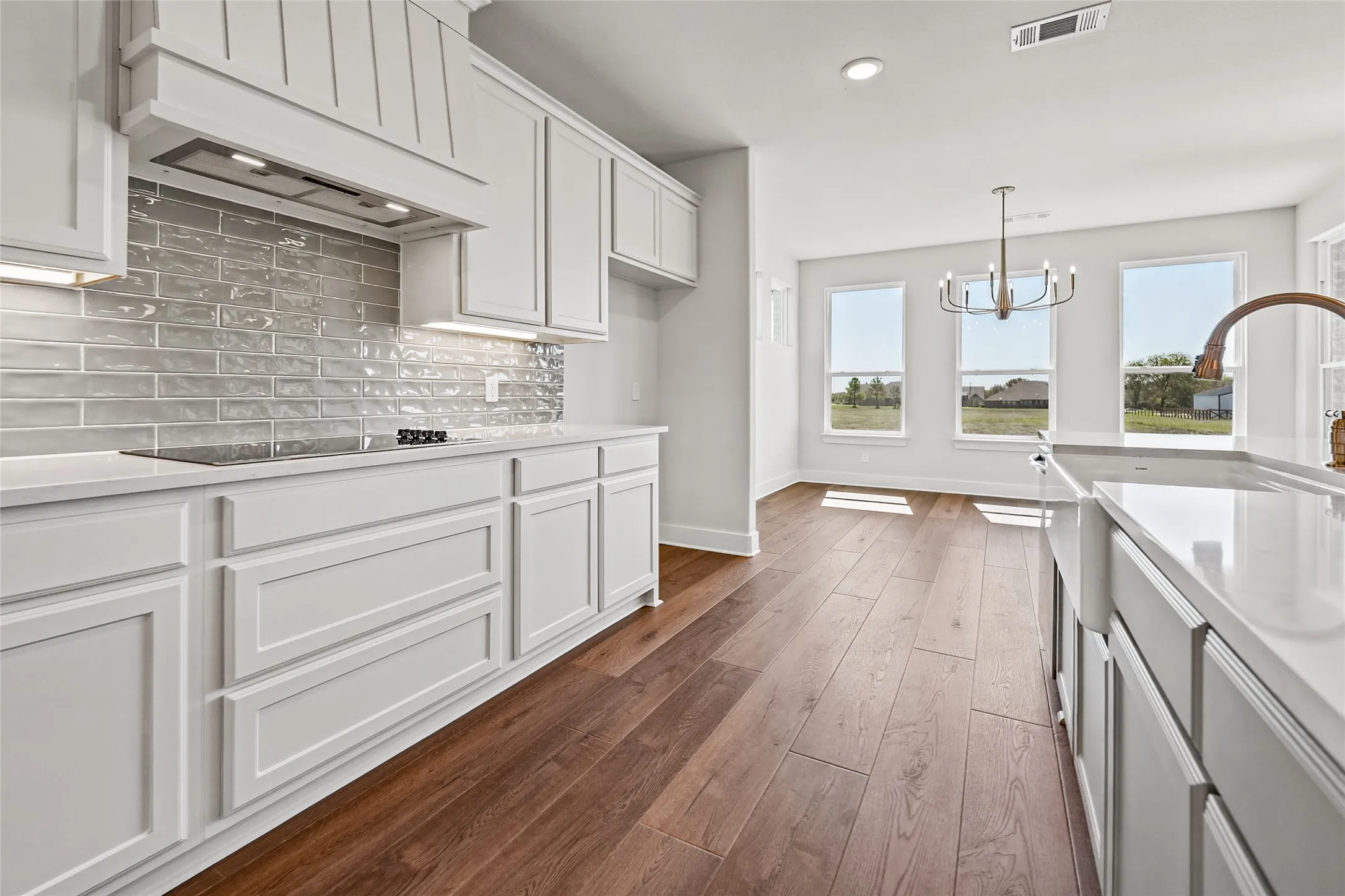 White shaker cabinetry, light-toned countertops, subway tile backsplash, wood-finish flooring, and a farmhouse sink