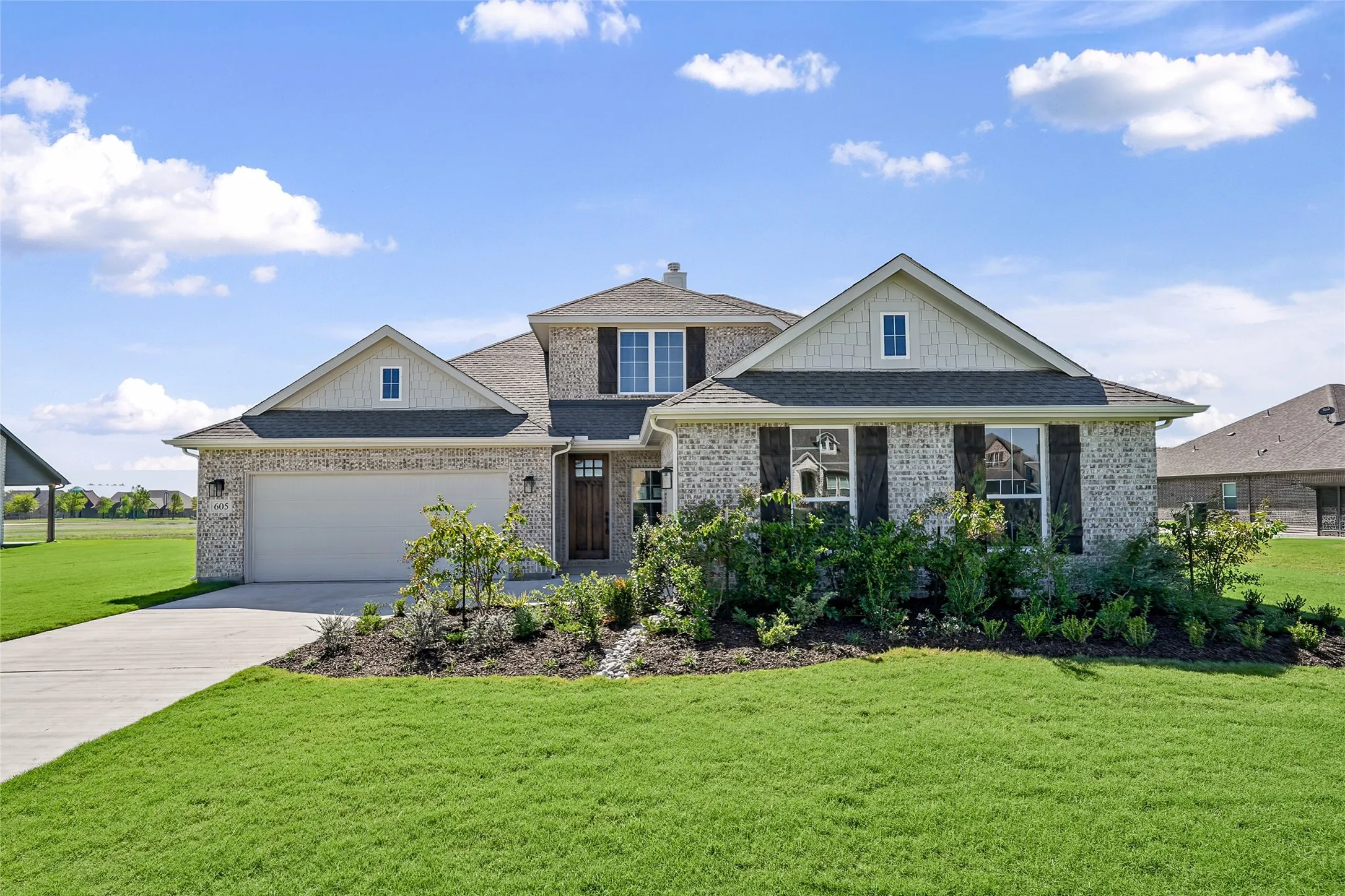 Brick and siding exterior featuring dark shutters, a front-entry garage, a concrete driveway, and established landscaping