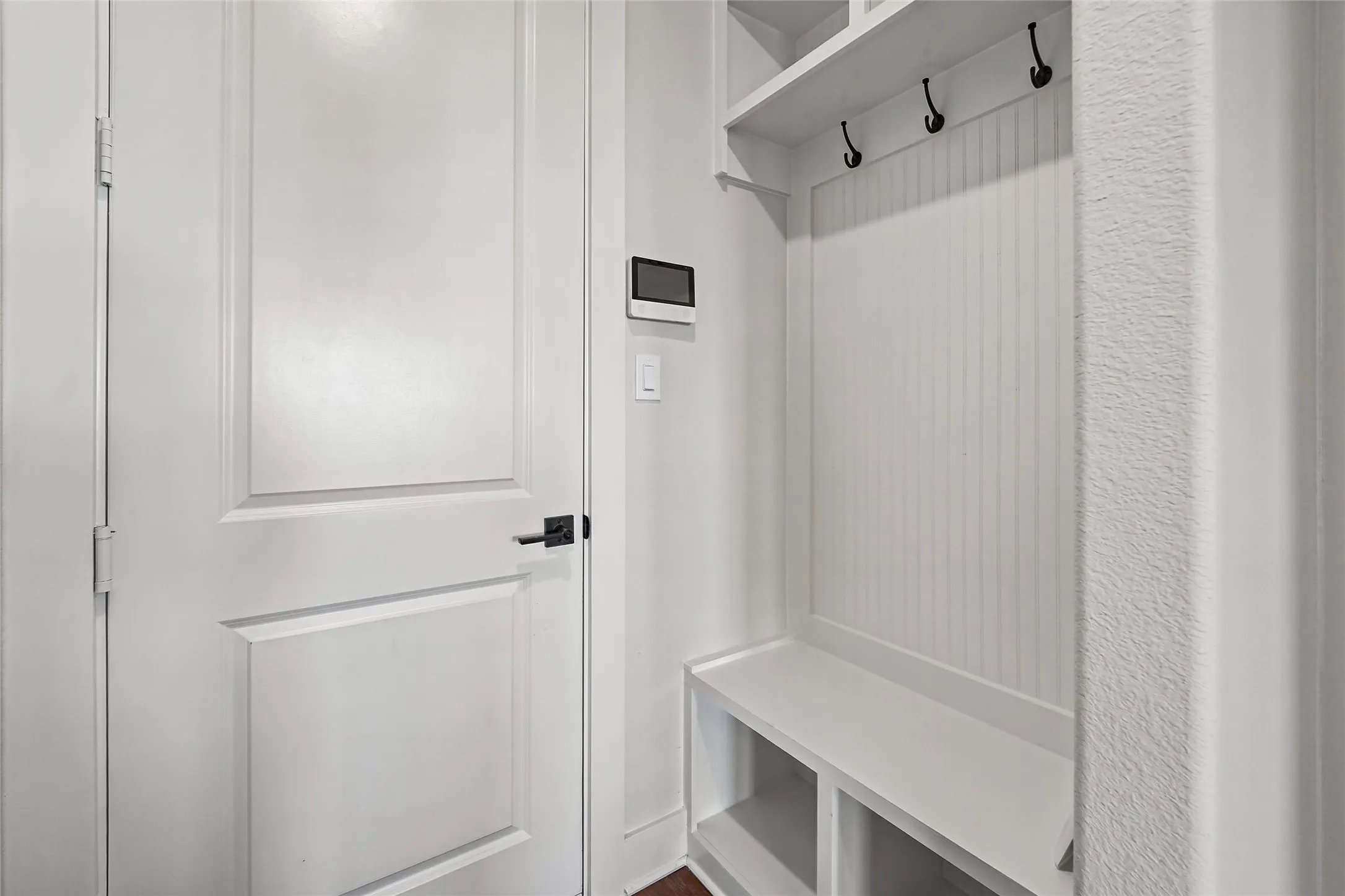 Built-in storage bench with cubbies, beadboard paneling, and upper shelving with hooks