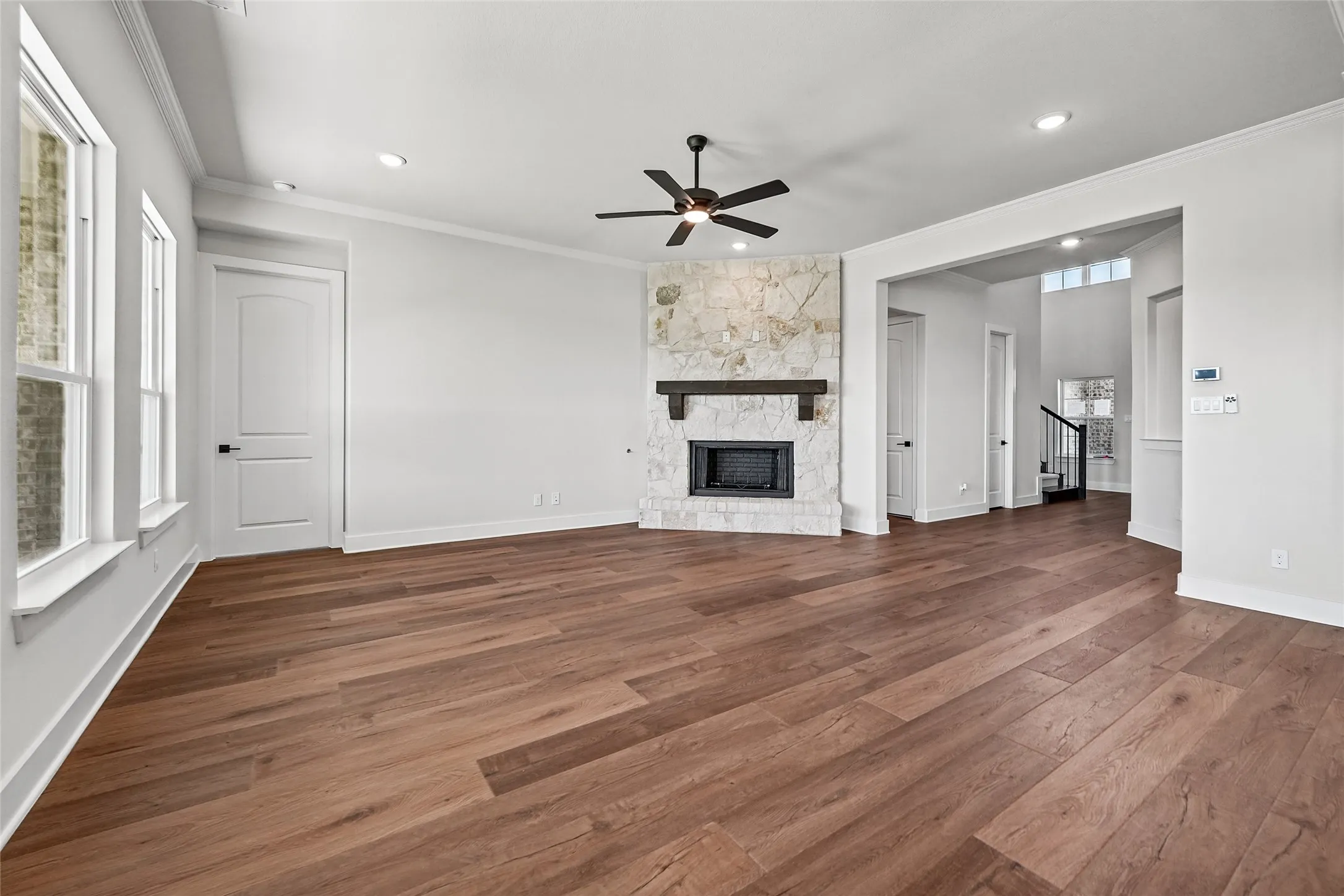 Wood-finish flooring, stone-clad fireplace with wood mantel, ceiling fan, recessed lighting, and white trim