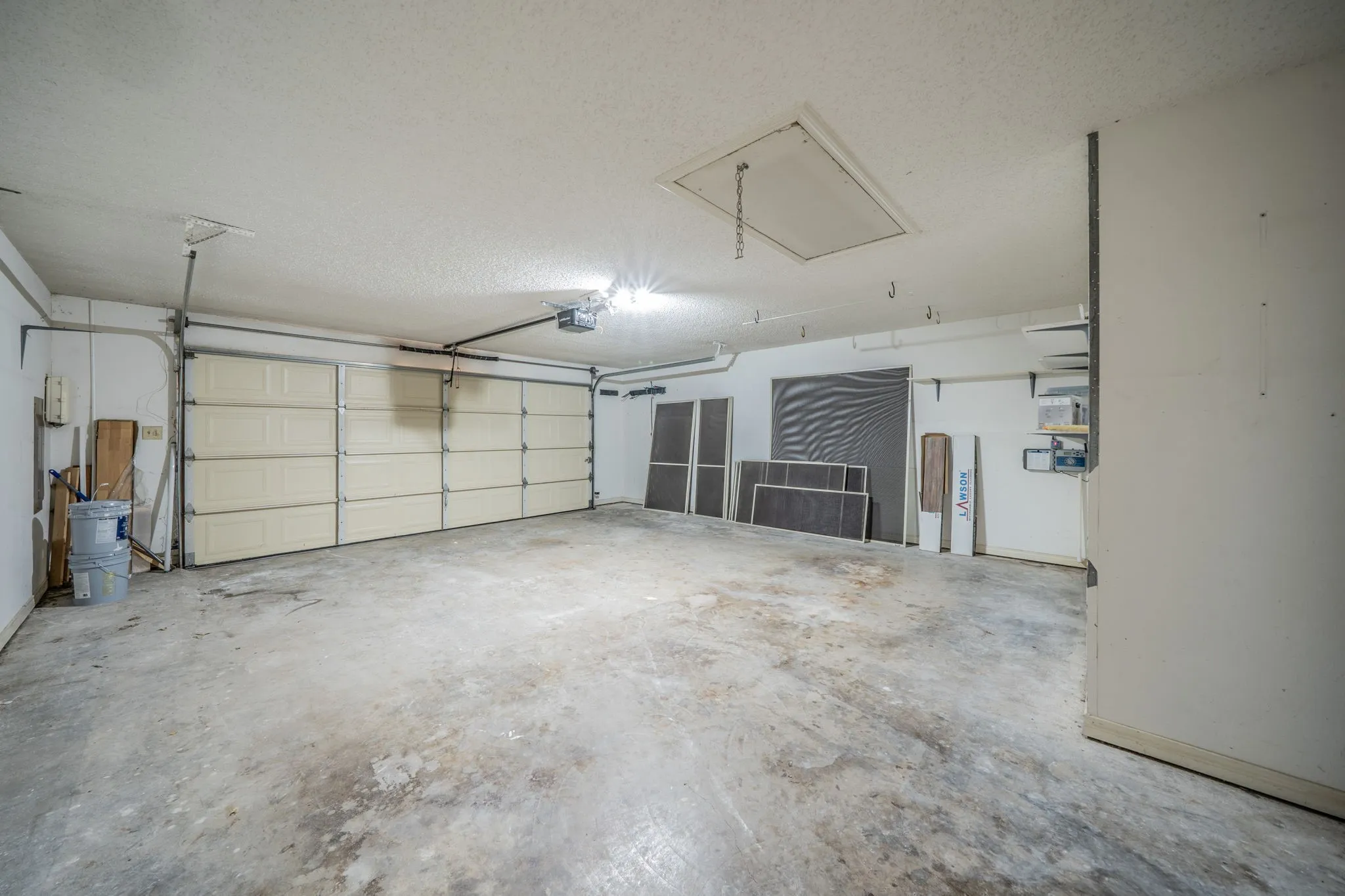 Spacious garage with concrete flooring, overhead lighting, and a paneled garage door