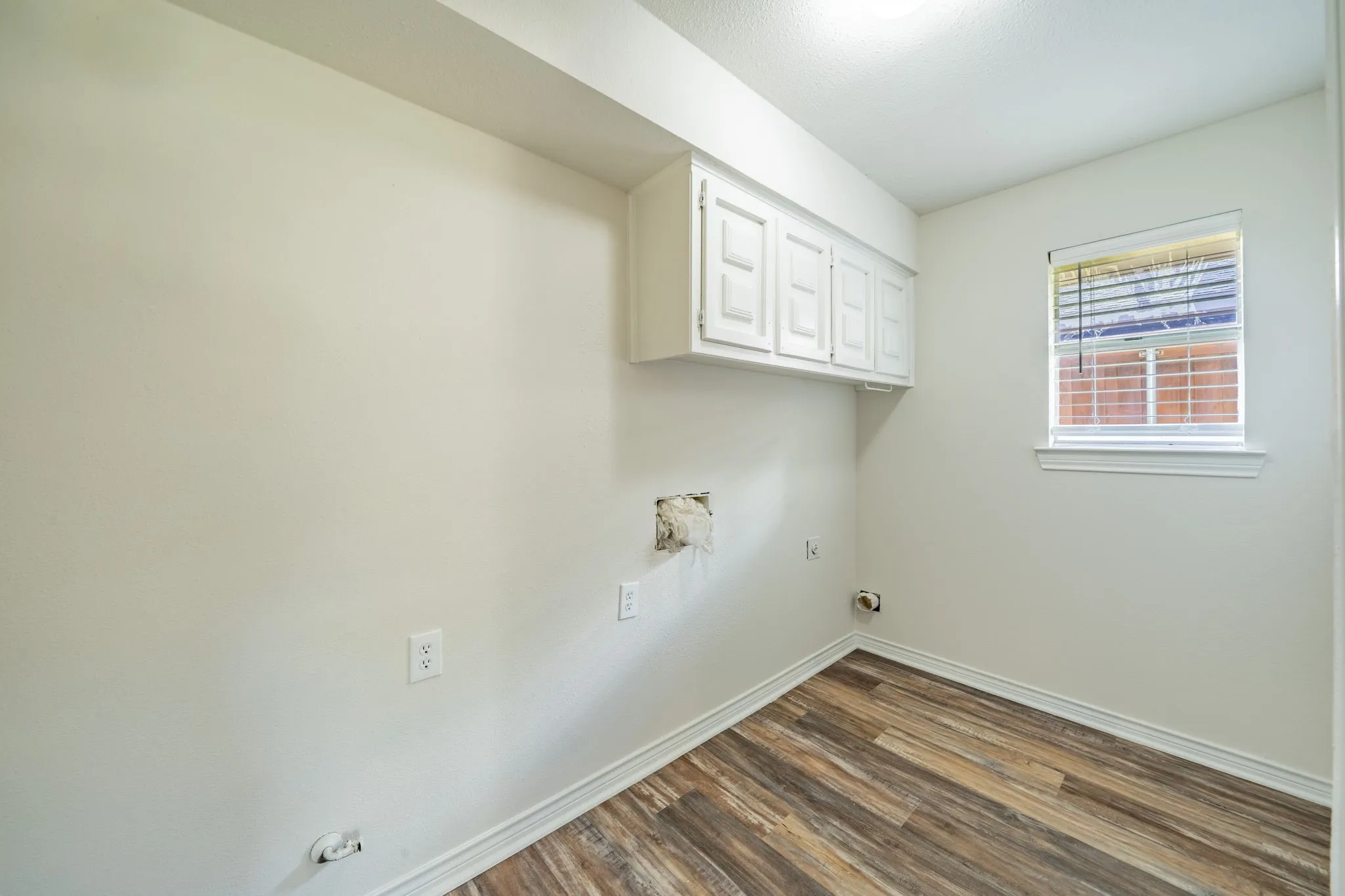 Laundry area with wood-finish flooring, white cabinetry, and a window with blinds