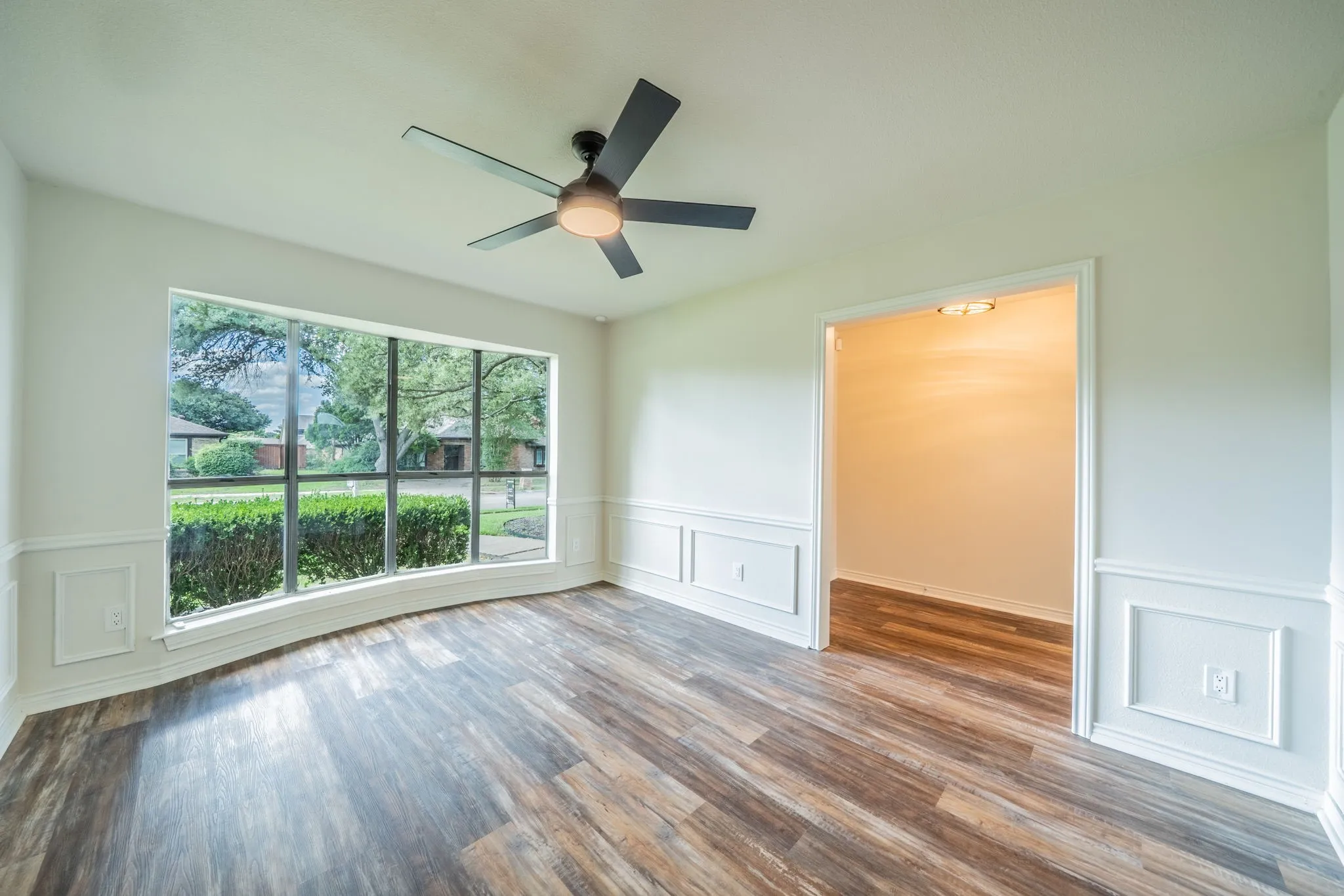 Spacious interior room featuring a large curved bay window, wood-finish flooring, and wainscoting