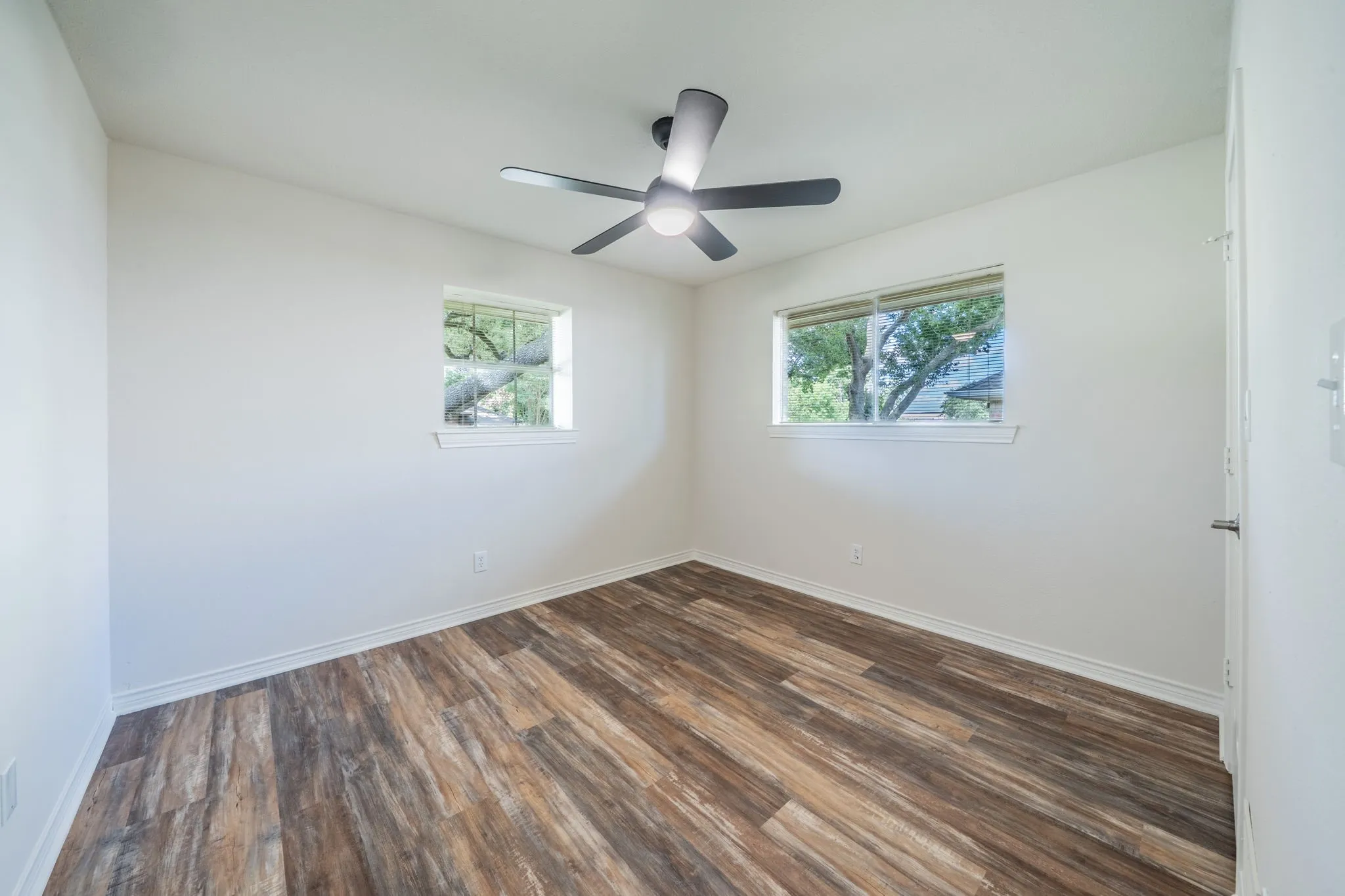 Interior room featuring two windows, wood-finish flooring, a contemporary ceiling fan, and white baseboards
