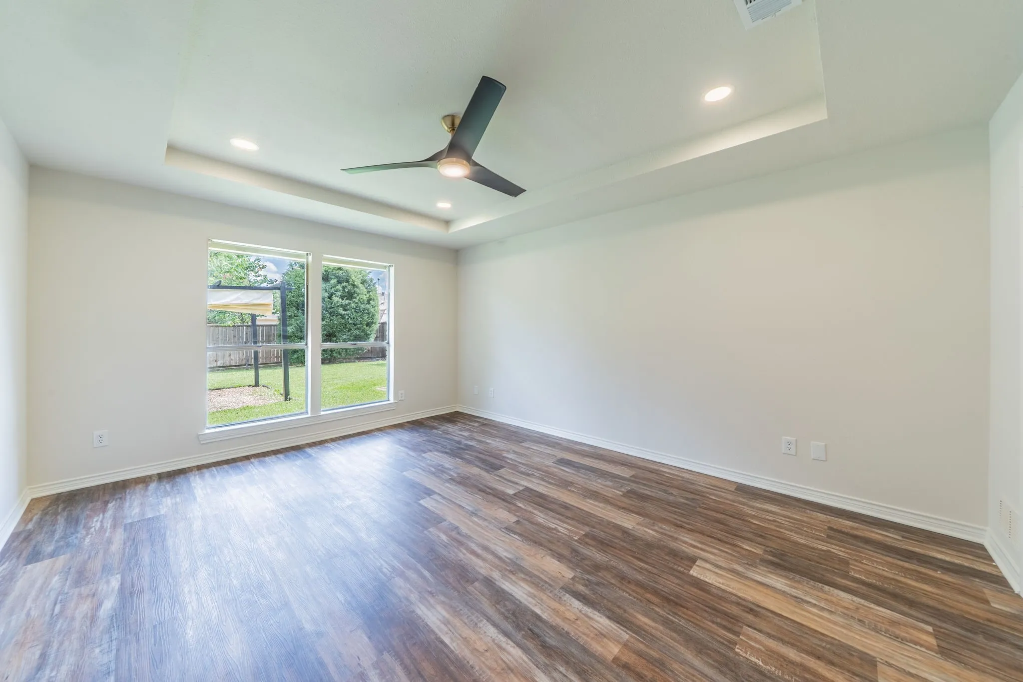Bright interior space featuring wood-finish flooring, a contemporary ceiling fan, and recessed lighting within a tray ceiling