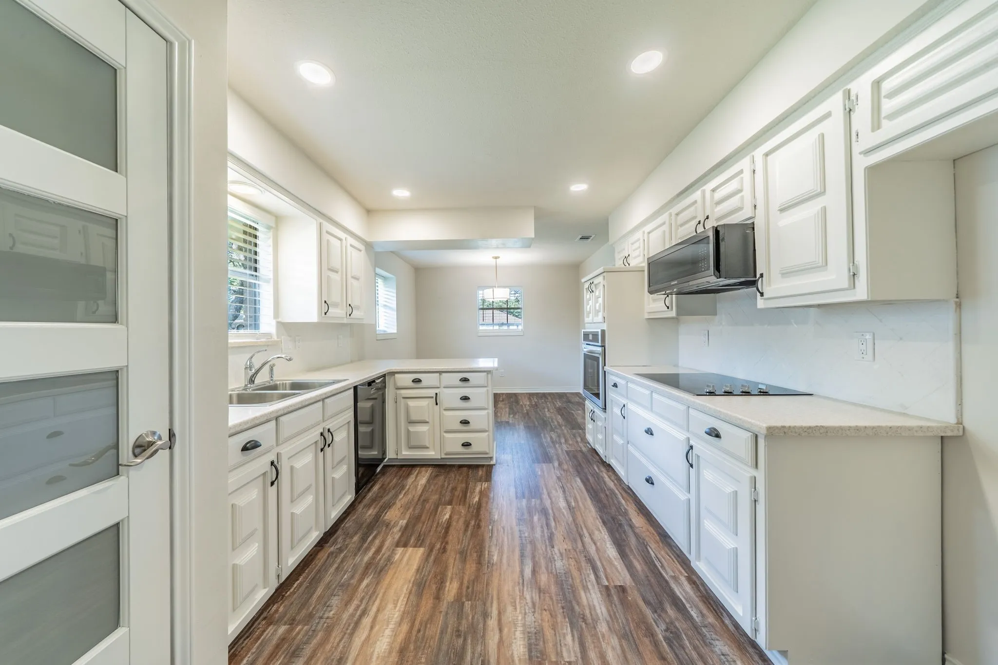 Kitchen featuring wood-finish flooring, white cabinetry, integrated stainless steel double sink, light-colored countertops, and recessed​​‌​​​​‌​​‌‌​‌‌​​​‌‌​‌​‌​‌​​​‌​​ lighting