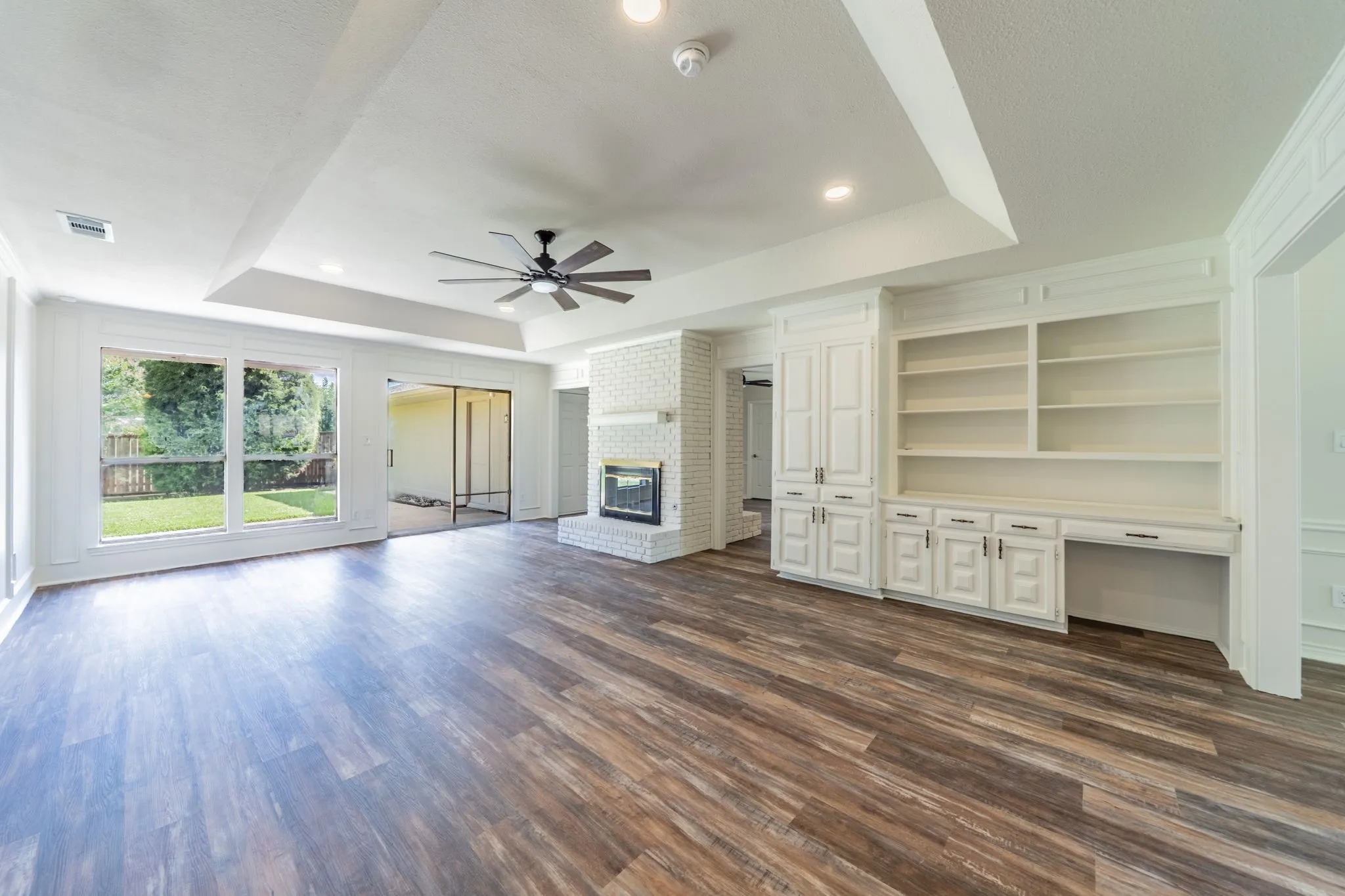 Spacious living area featuring wood-finish flooring, a white brick fireplace, and built-in cabinetry with shelving