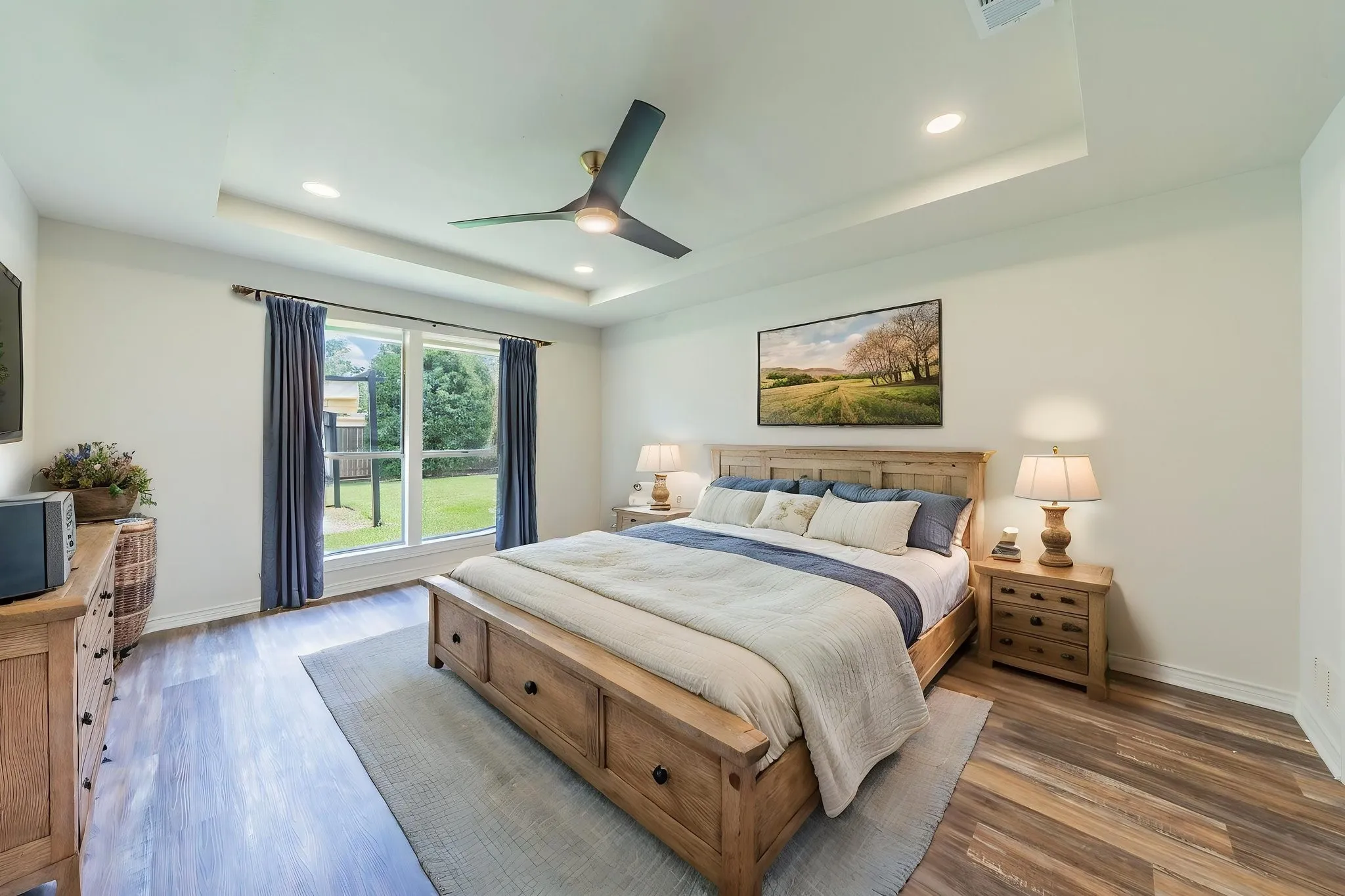 Virtually Staged. Spacious room featuring wood-finish flooring, a tray ceiling with recessed lighting, and a modern ceiling fan