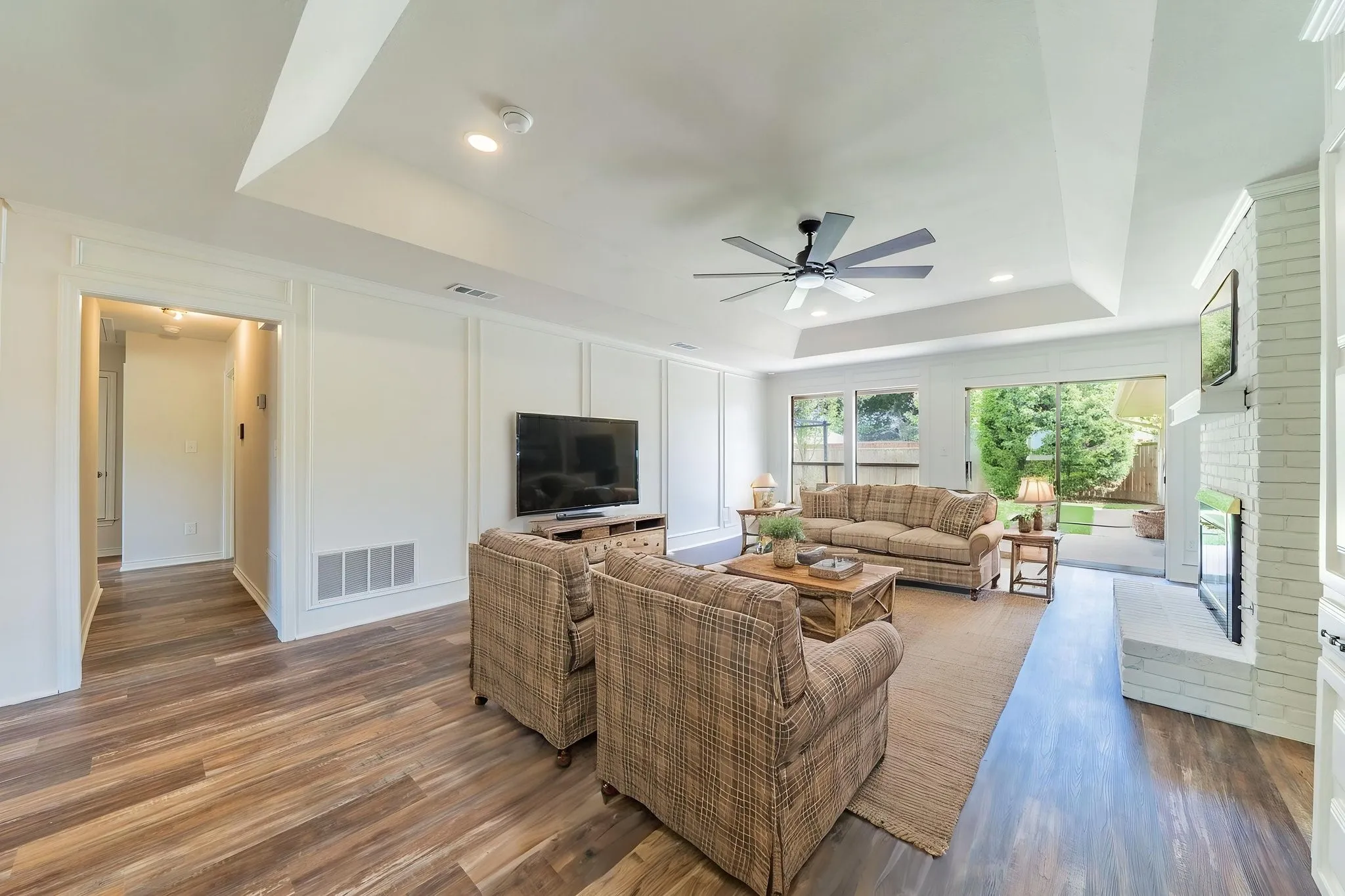 Virtually Staged. Living area featuring wood-finish flooring, a tray ceiling with a ceiling fan, and recessed lighting