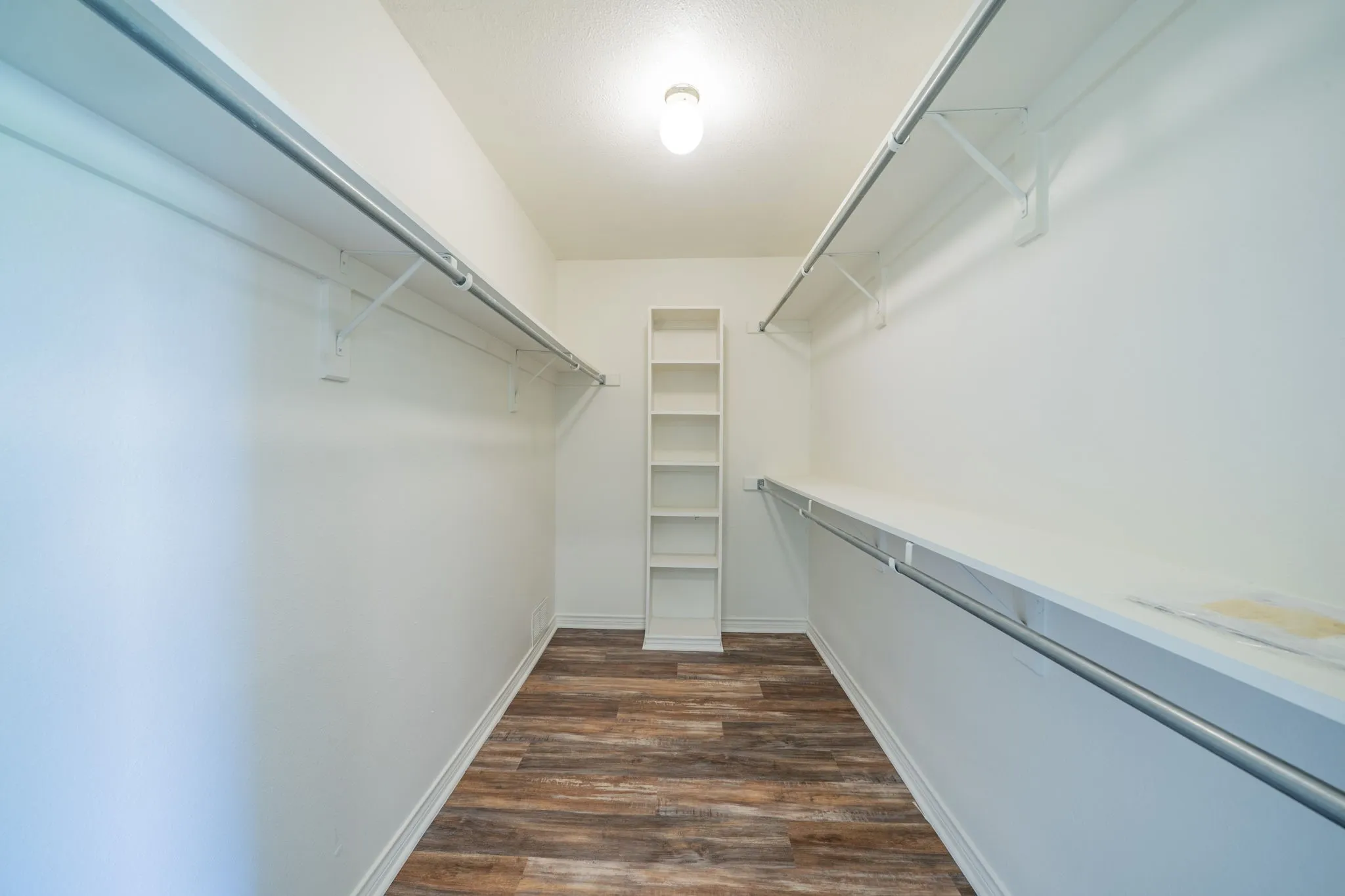 Spacious walk-in closet featuring wood-finish flooring, white shelving, and dual hanging rods
