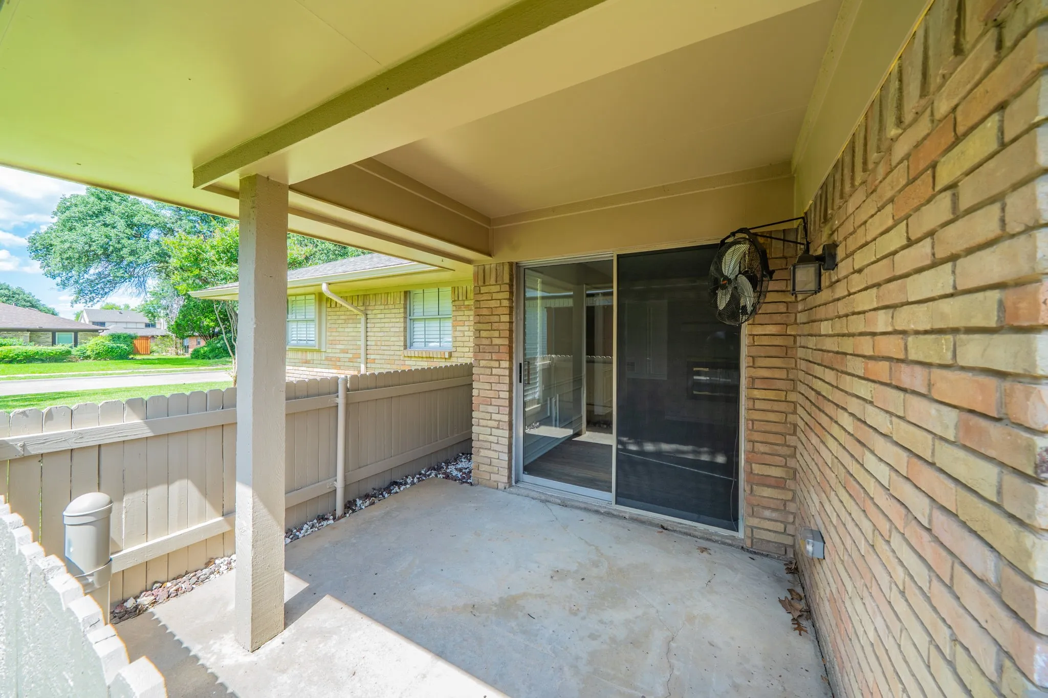 Covered side patio area featuring a concrete slab, brick exterior wall, and a sliding glass door with a screen