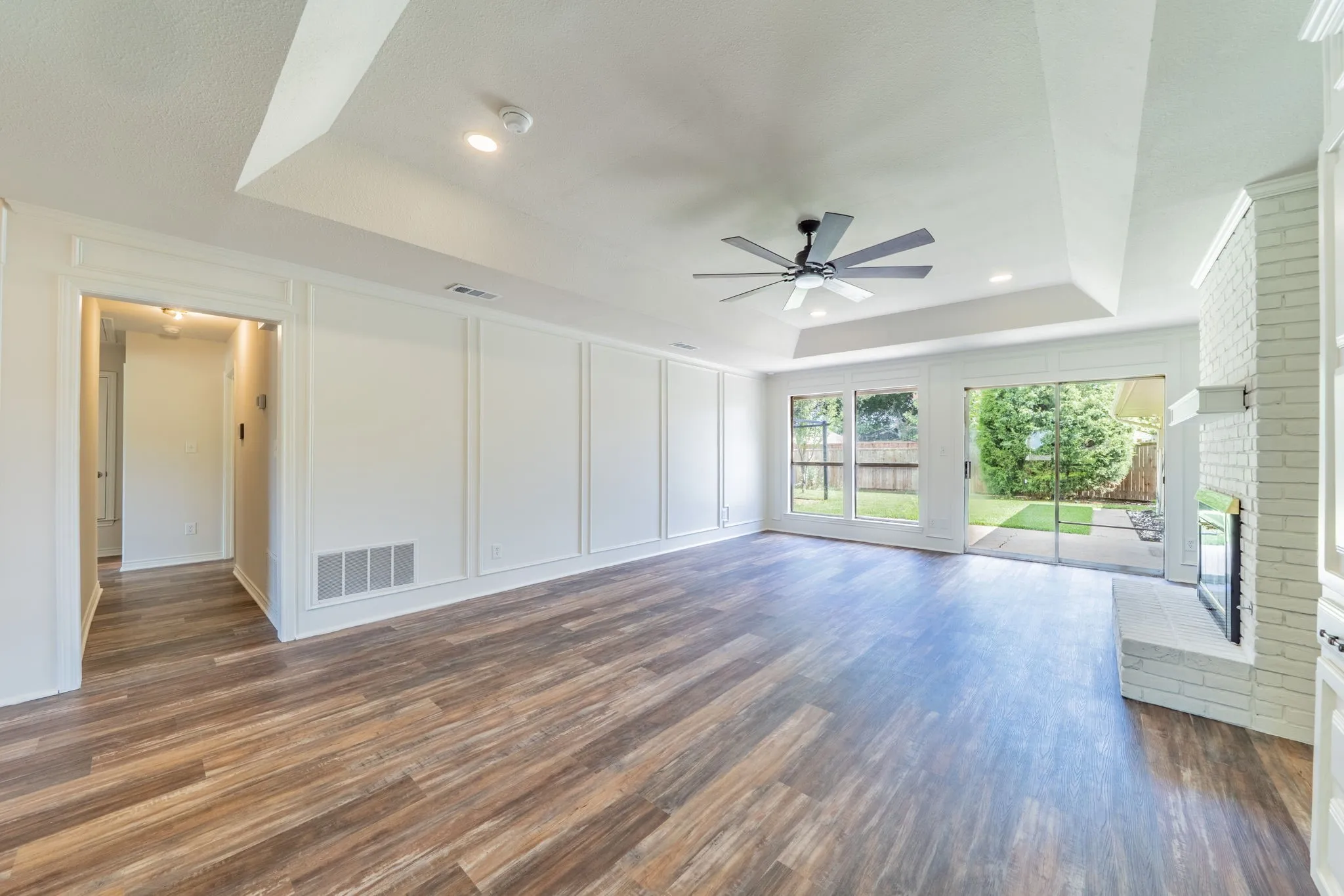 Spacious living area featuring wood-finish flooring, white panel molding, and a tray ceiling with recessed lighting