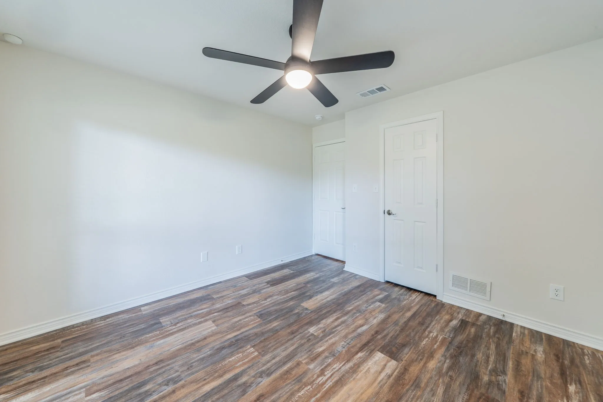 Spacious room with wood-finish flooring, crisp white walls, and a contemporary ceiling fan