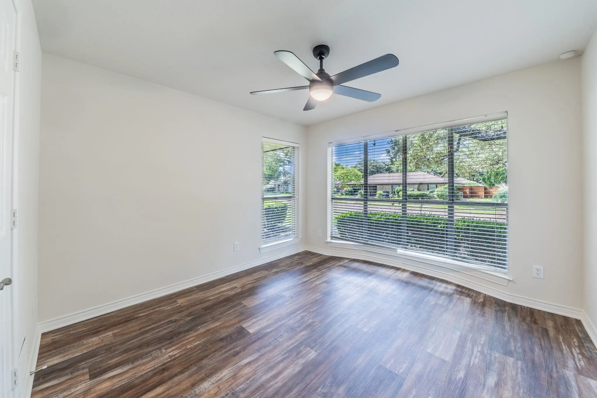Spacious room featuring wood-finish flooring, white walls, and a ceiling fan with integrated lighting
