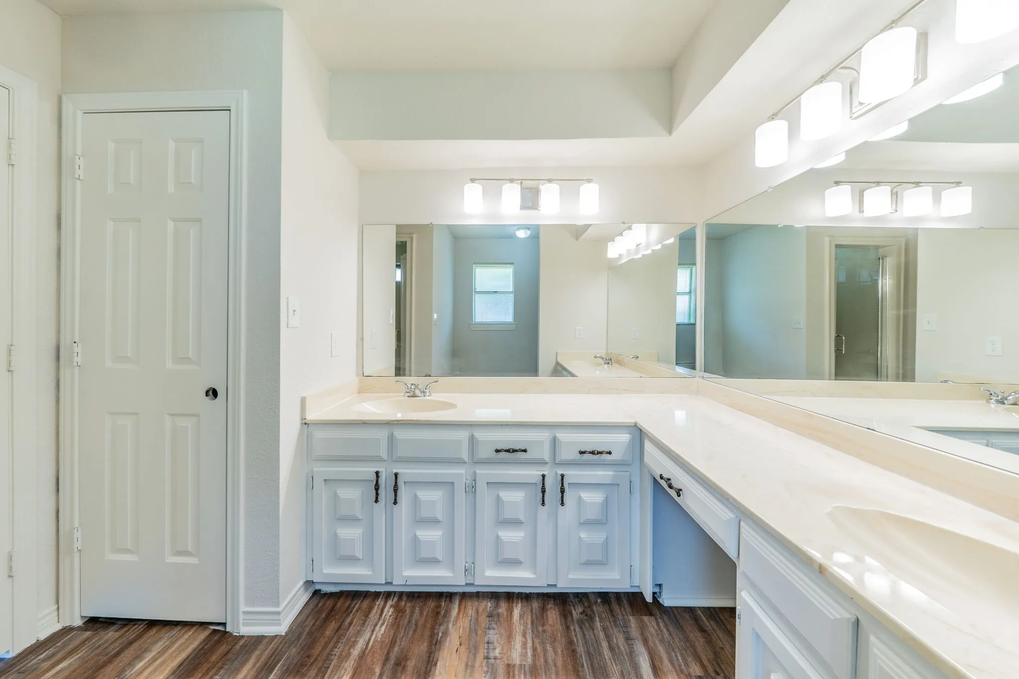 Bathroom vanity area featuring dual sinks set within a light-toned countertop, extensive wall-mounted mirrors, and wood-finish flooring